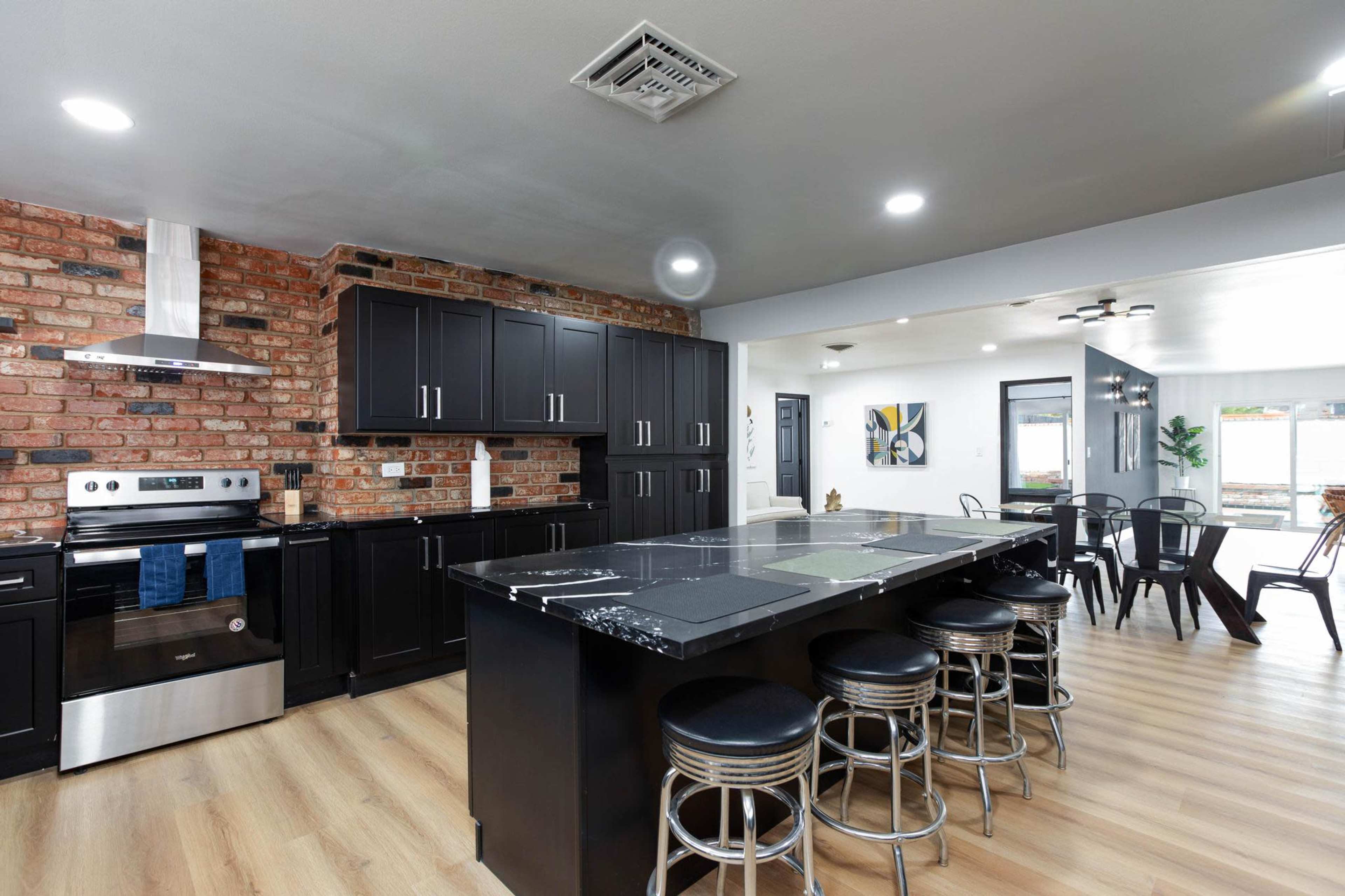The kitchen features a brick accent wall, dark cabinetry, a stainless steel oven, and a large island with seating.