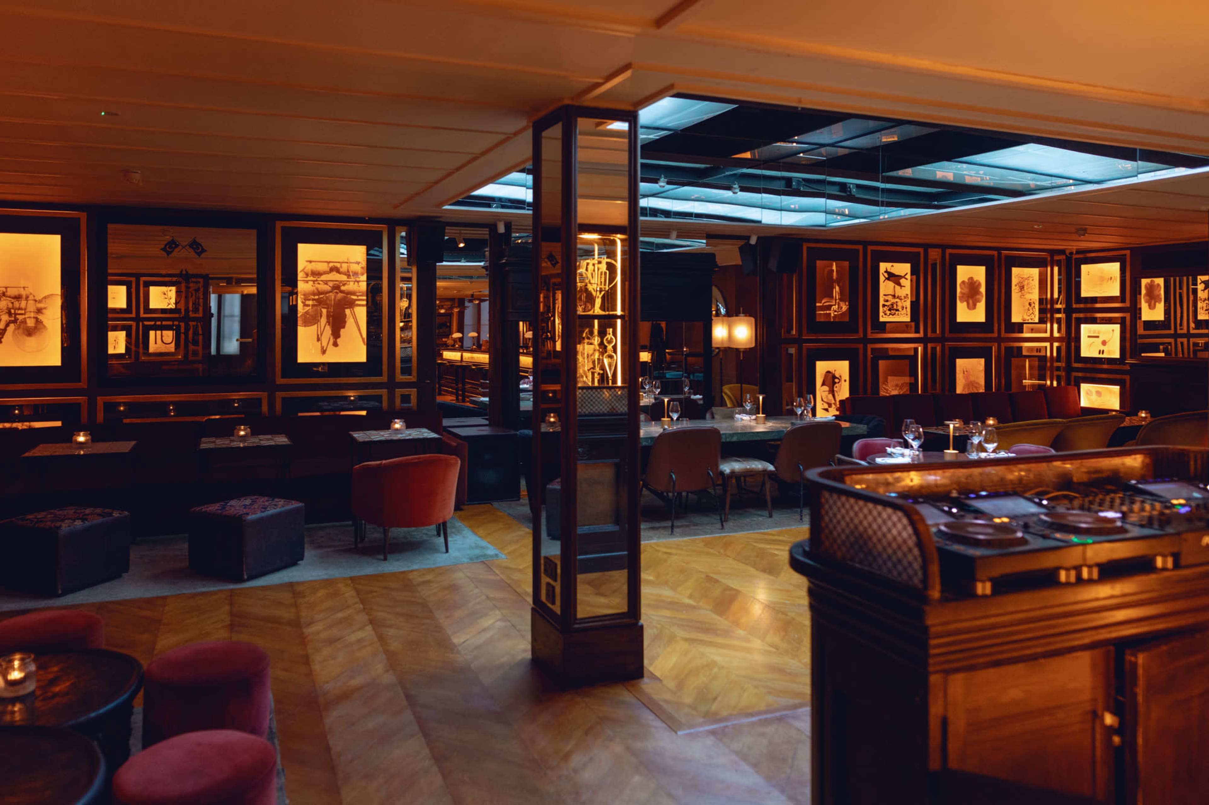 The interior of a restaurant featuring wooden flooring, framed artwork on the walls, and various seating options.