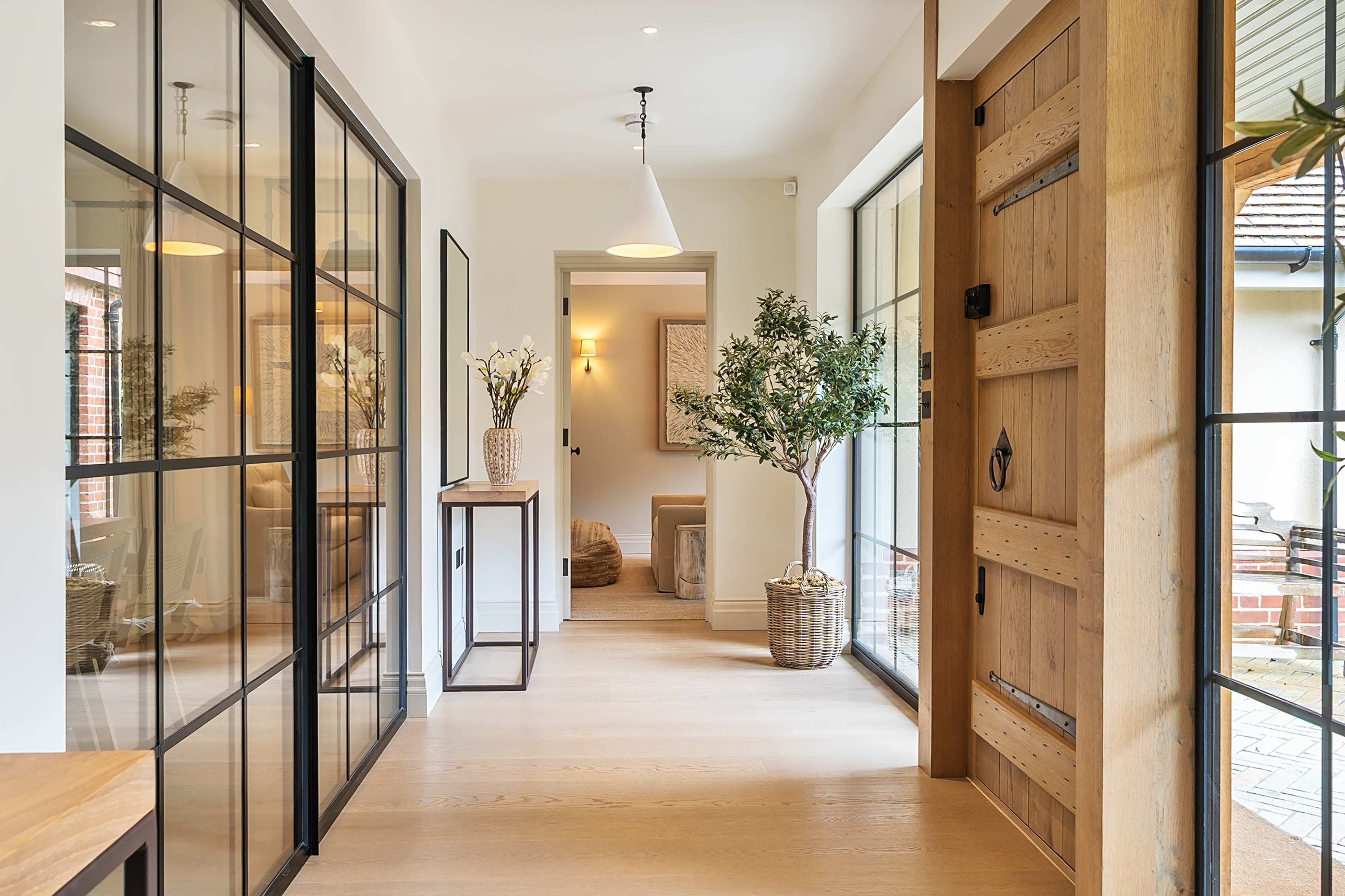 The image shows a modern entrance hallway with large glass doors, wooden accents, and decorative plants.