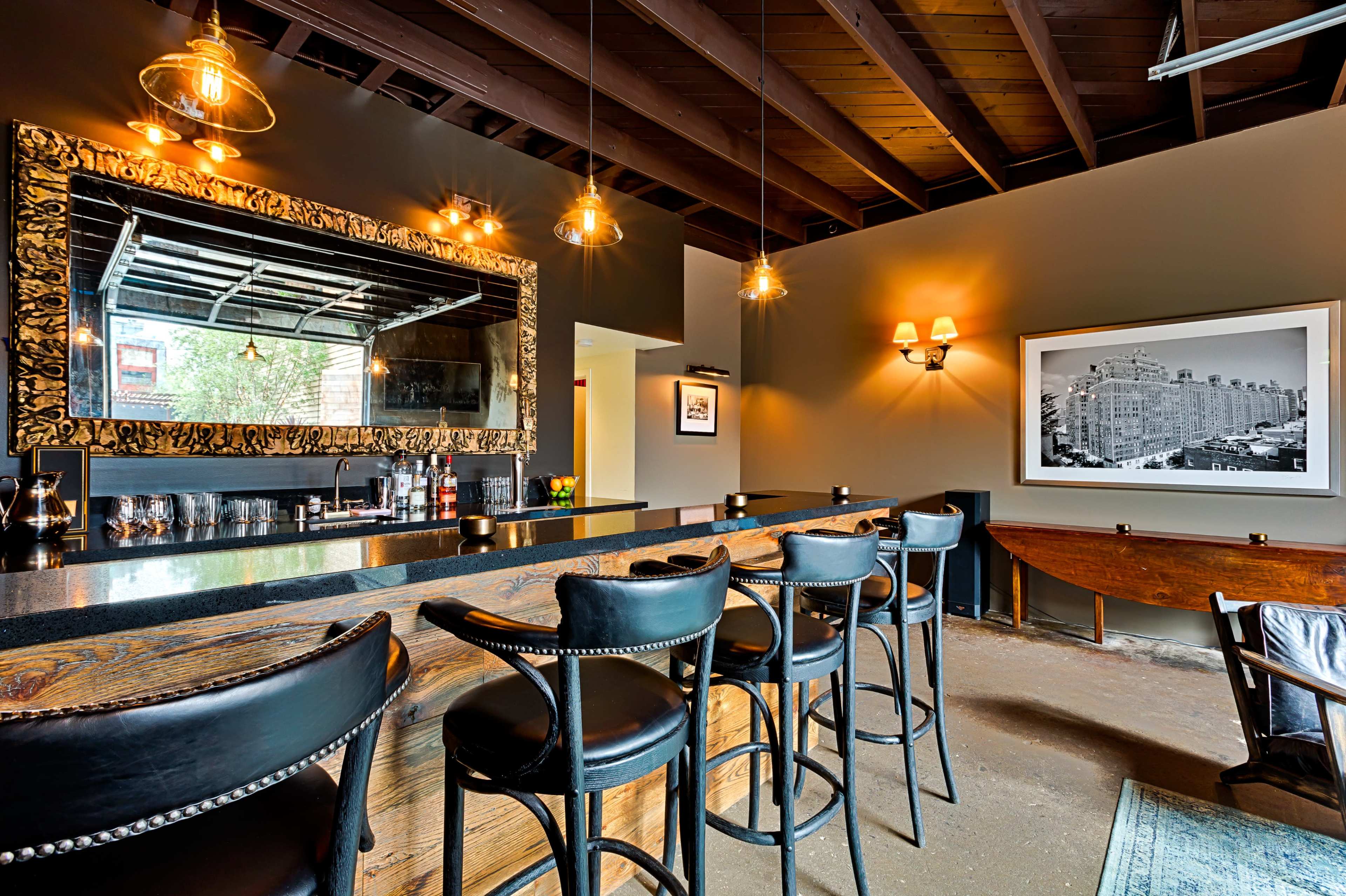The image shows a sophisticated bar area with high-backed black chairs, a large ornate mirror, and stylish lighting fixtures.