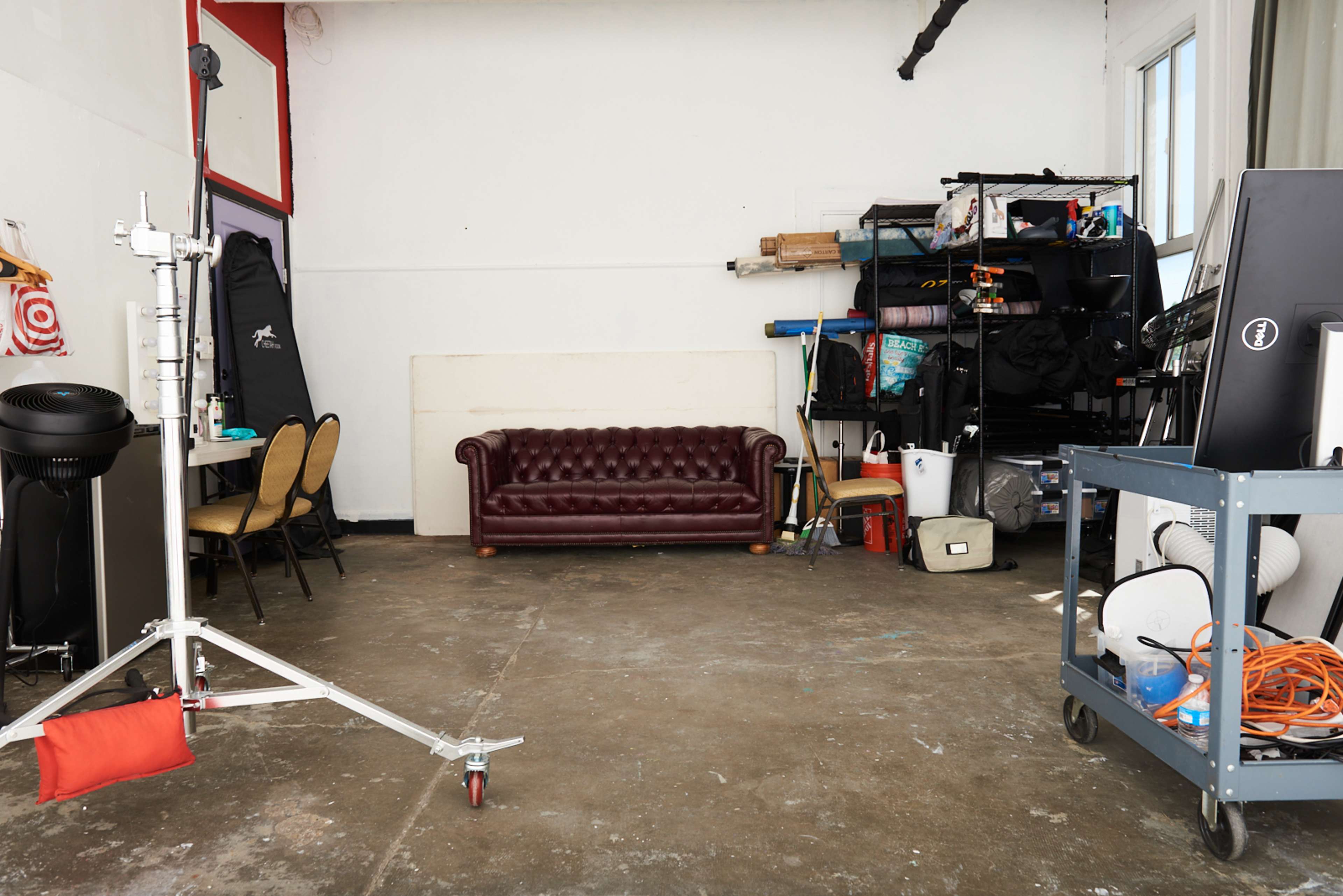 An empty studio space with a brown leather sofa, shelves filled with equipment, and furniture arranged along the walls.