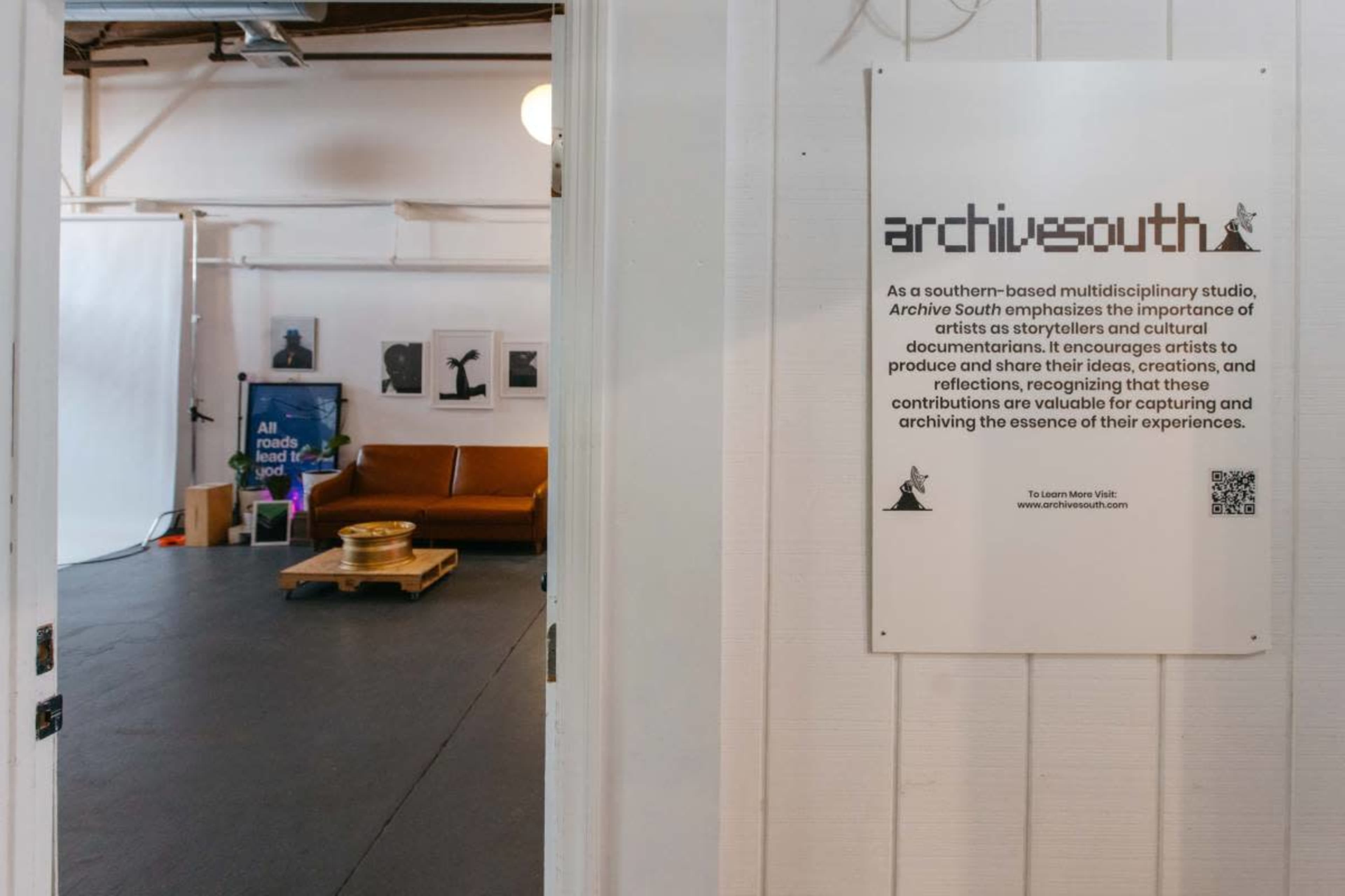 The image shows a creative studio space with a sign about Archive South, a brown couch, and artistic prints on the walls.