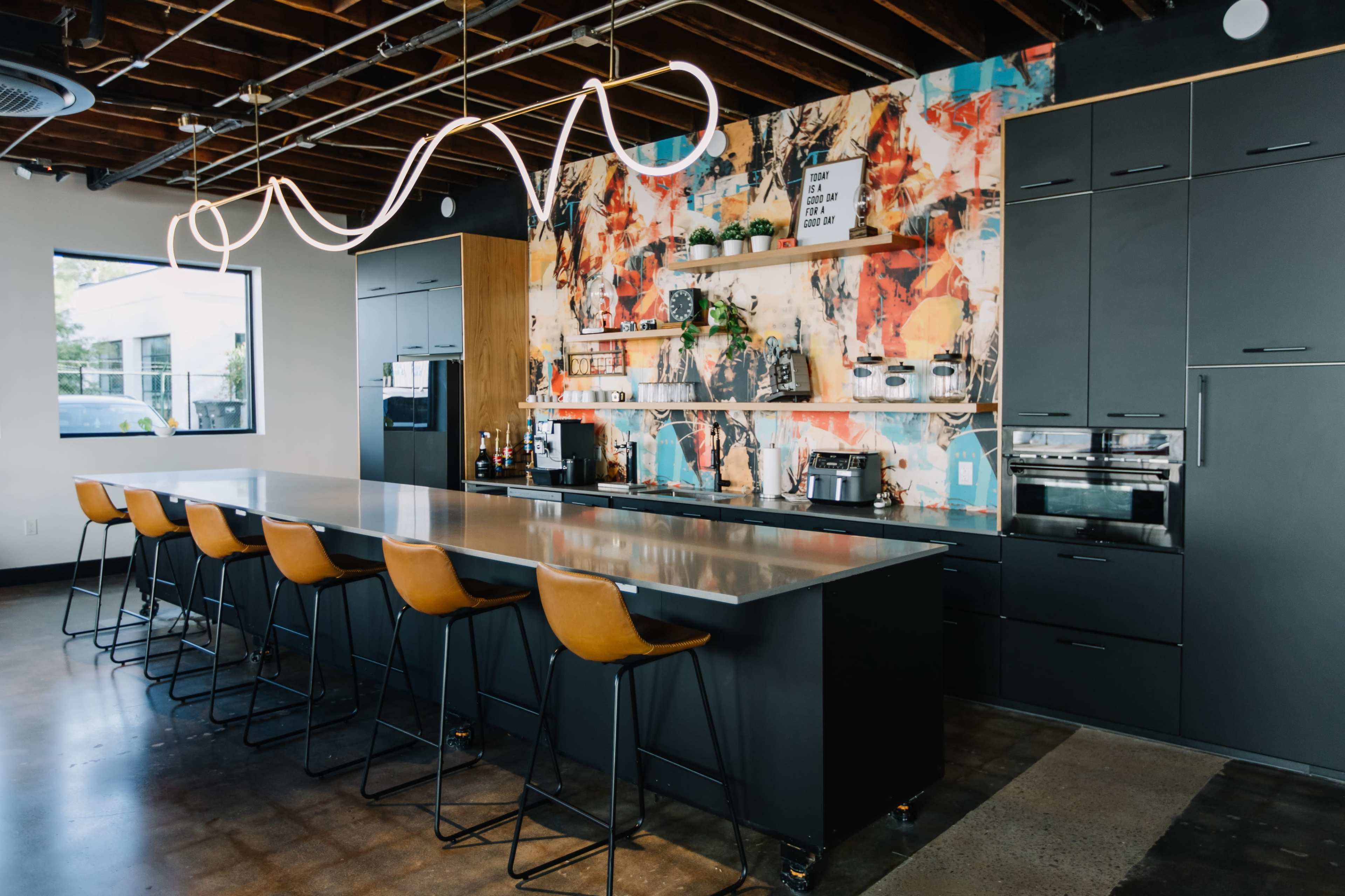 The image shows a modern kitchen with a large metallic island, bar stools, and a colorful abstract mural on the wall.