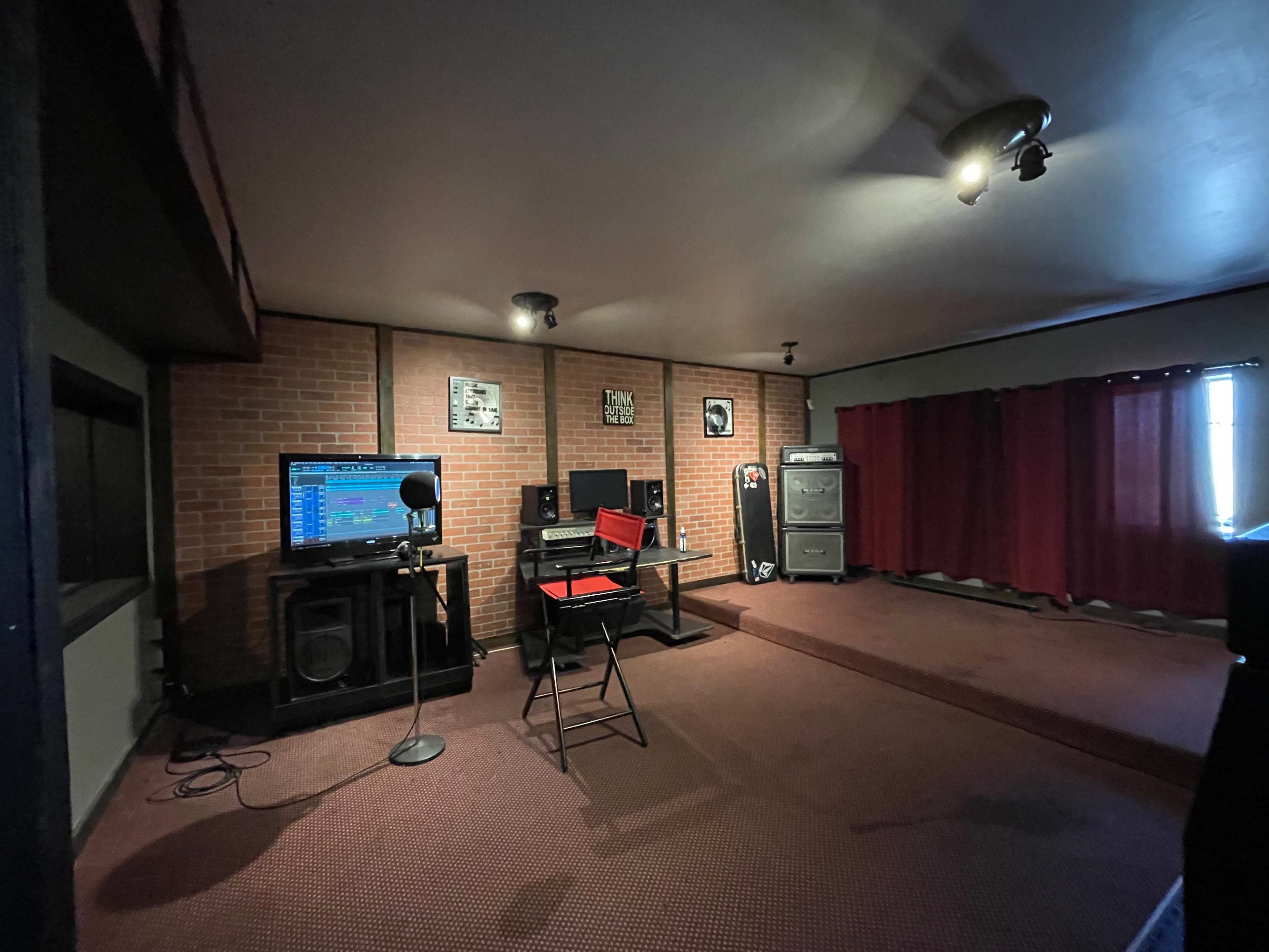 A recording studio with a brick wall, a computer setup for music production, speakers, and a microphone on a stand.