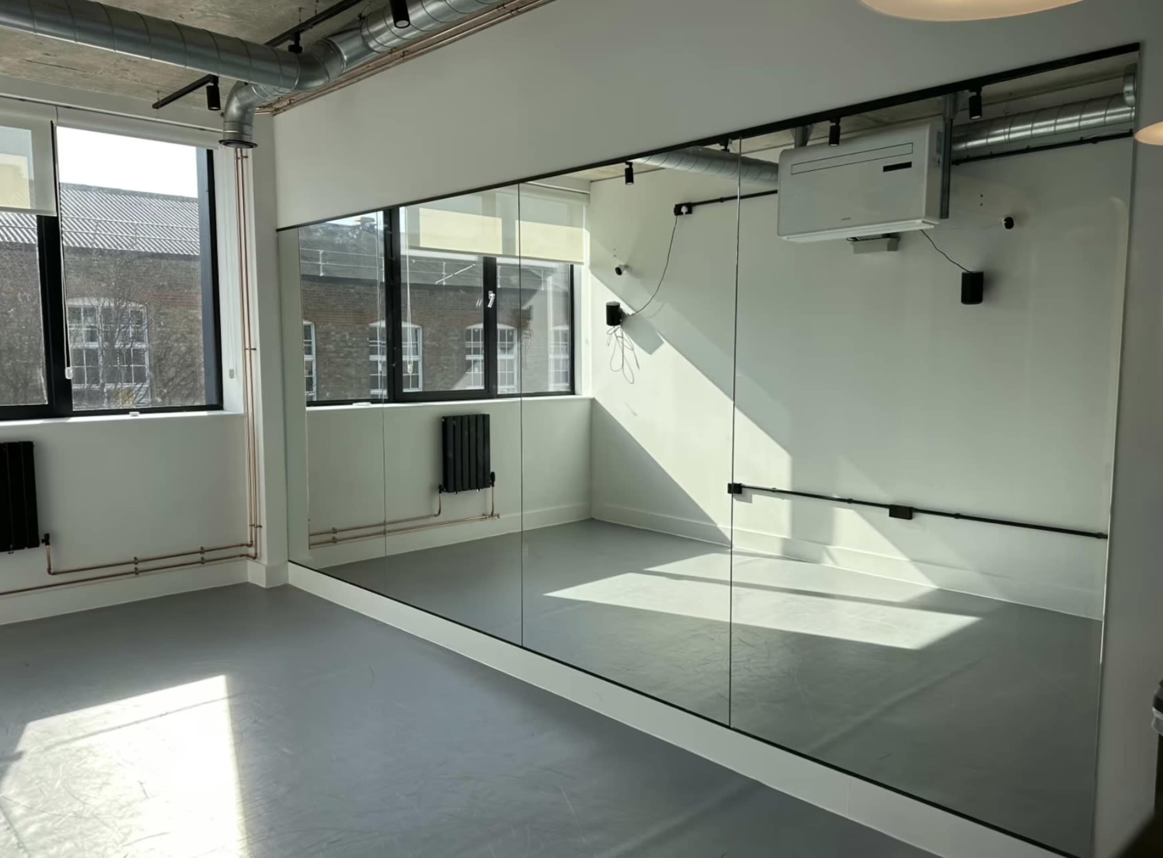 The image shows a sunlit room with a large mirror on one wall and windows providing natural light.