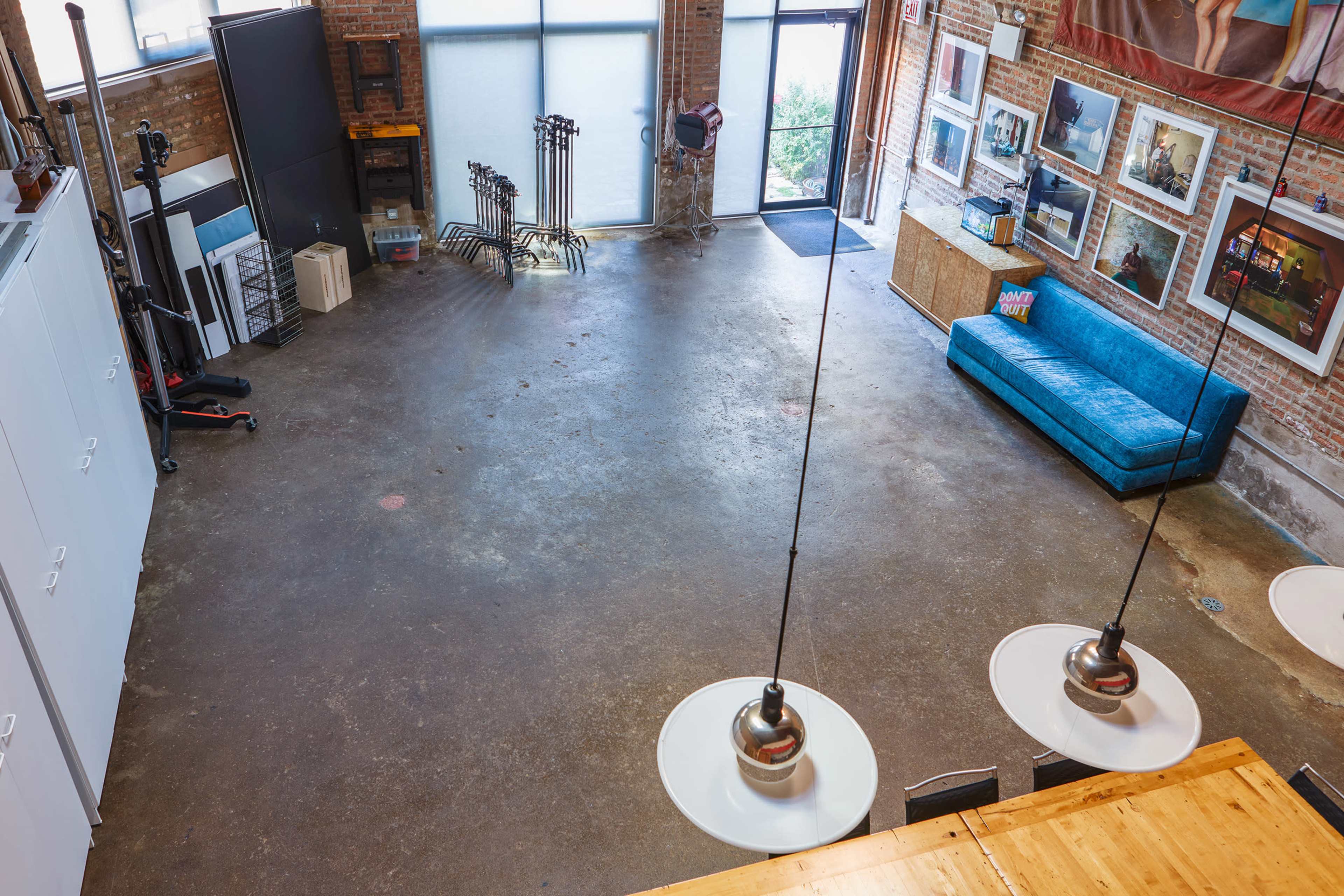 An open, industrial space with a concrete floor, a turquoise sofa, and large windows letting in natural light.