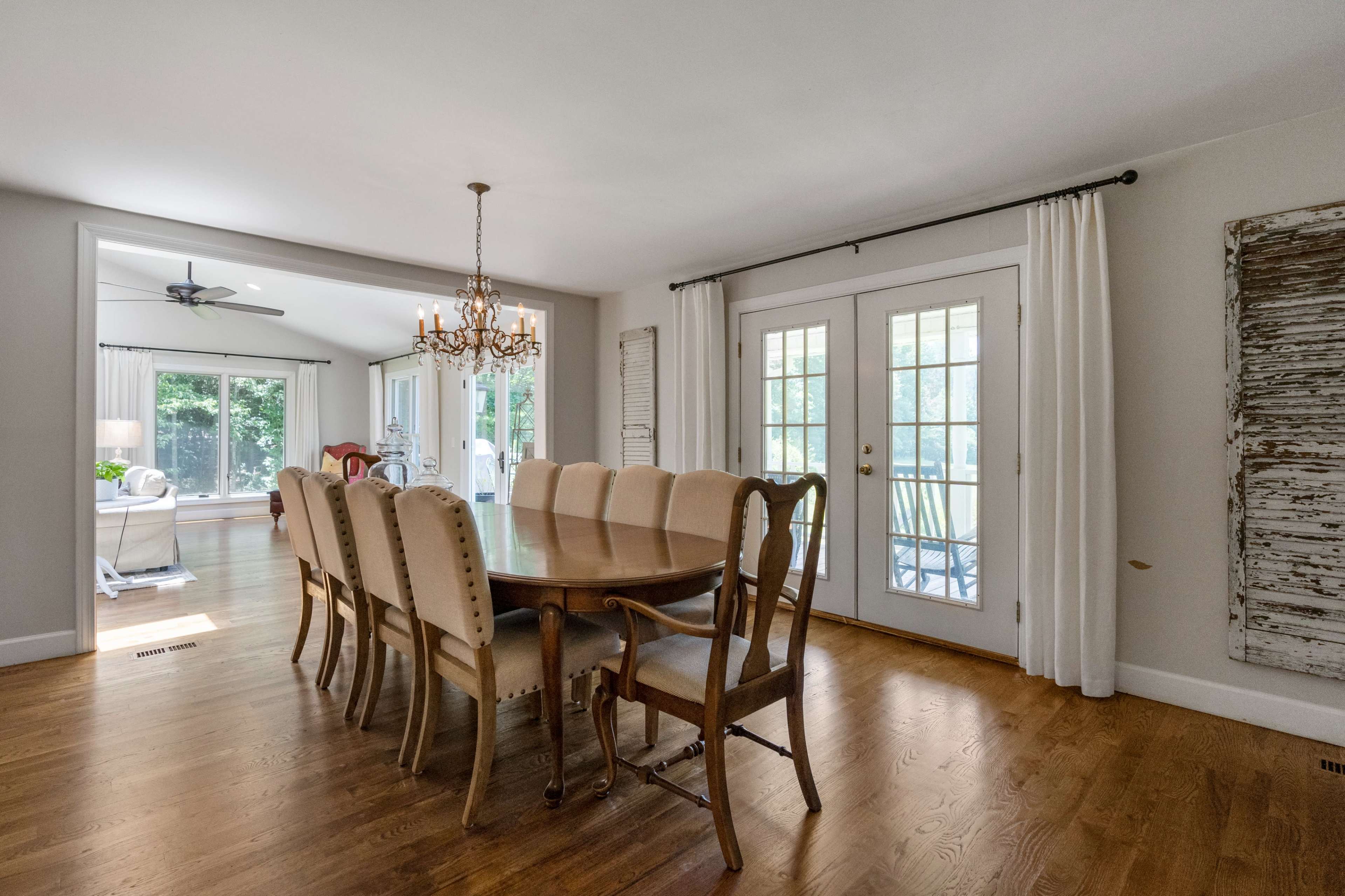 A spacious dining room features a large wooden table surrounded by upholstered chairs, leading to a set of glass doors that open to an outdoor area.