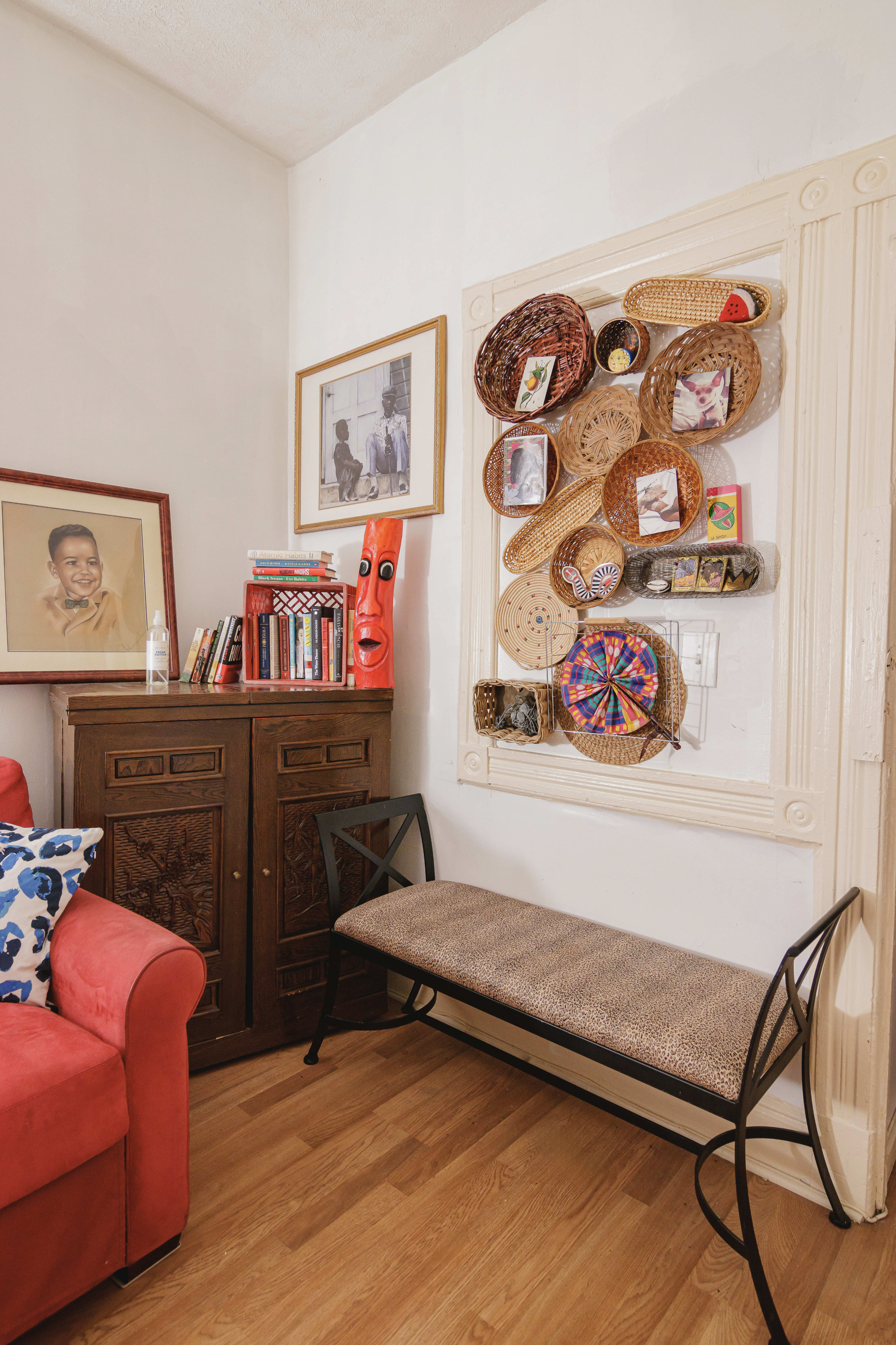 A cozy corner of a room with a red couch, an antique wooden cabinet, a framed photo, and decorative woven baskets mounted on the wall.