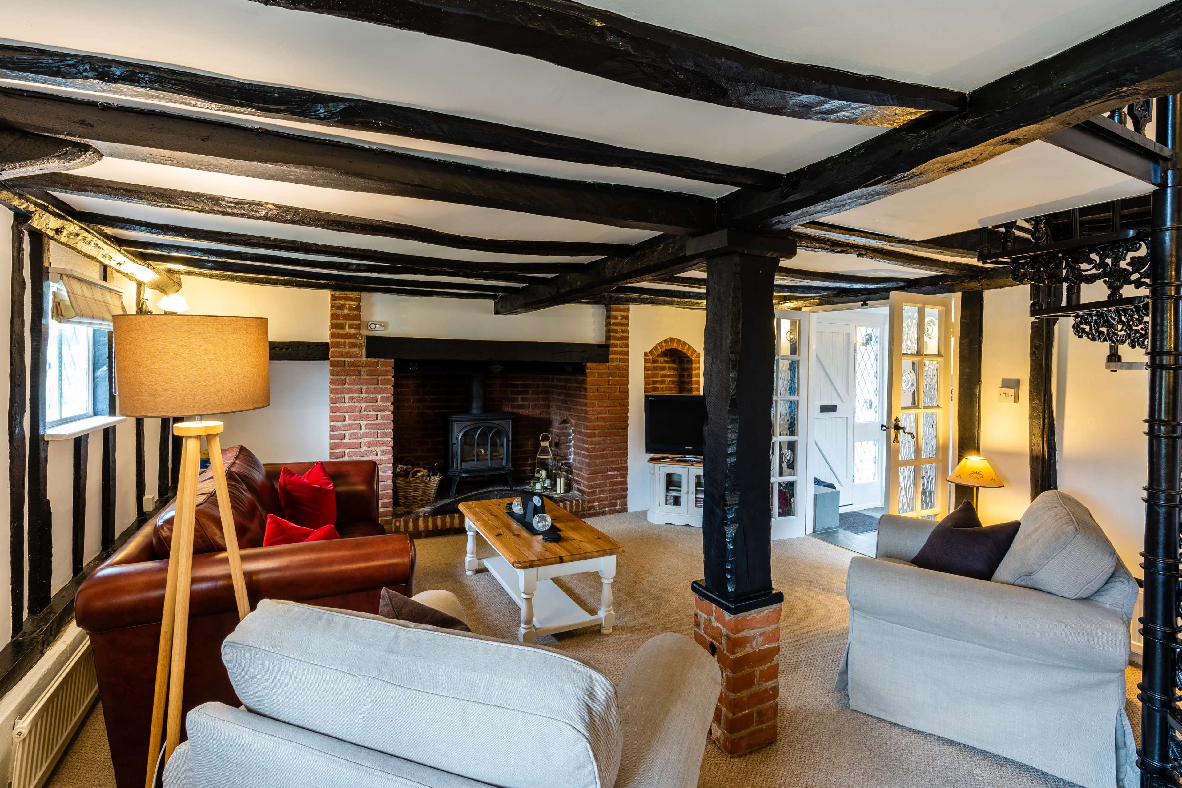 A cozy living room features exposed wooden beams, a brick fireplace, and comfortable seating arranged around a central coffee table.