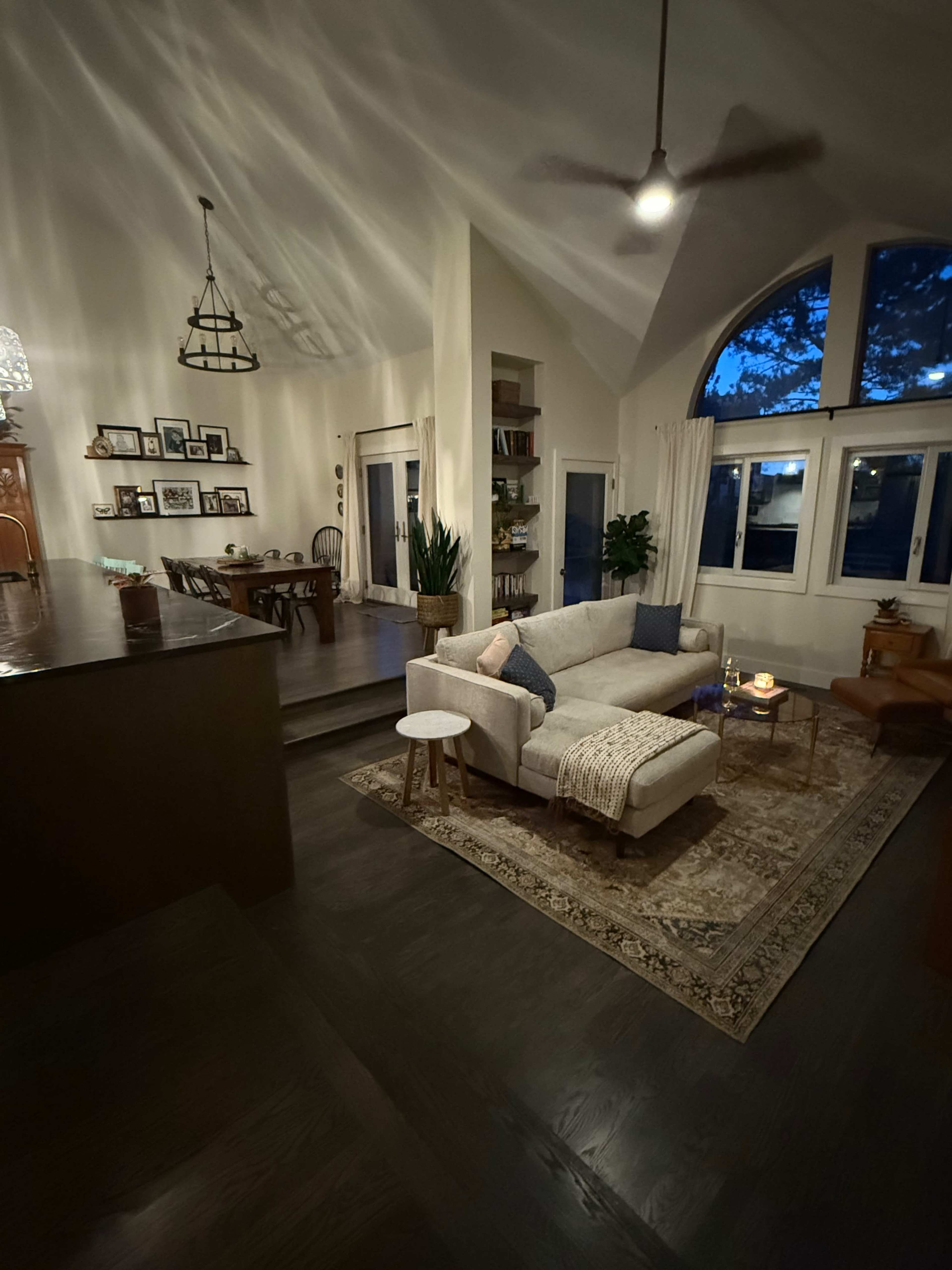 The image shows a modern living room with a light-colored sectional sofa, a coffee table, and a large window allowing dim natural light to enter.
