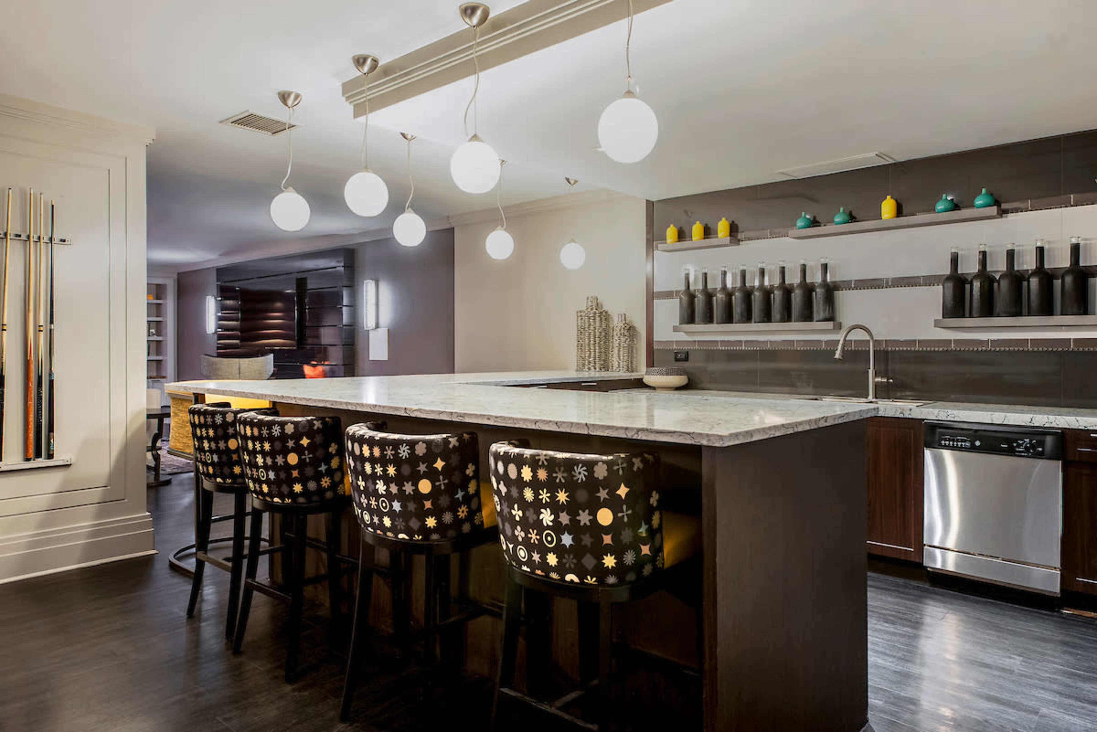 A modern kitchen with a long countertop, four bar stools, and hanging circular light fixtures above.