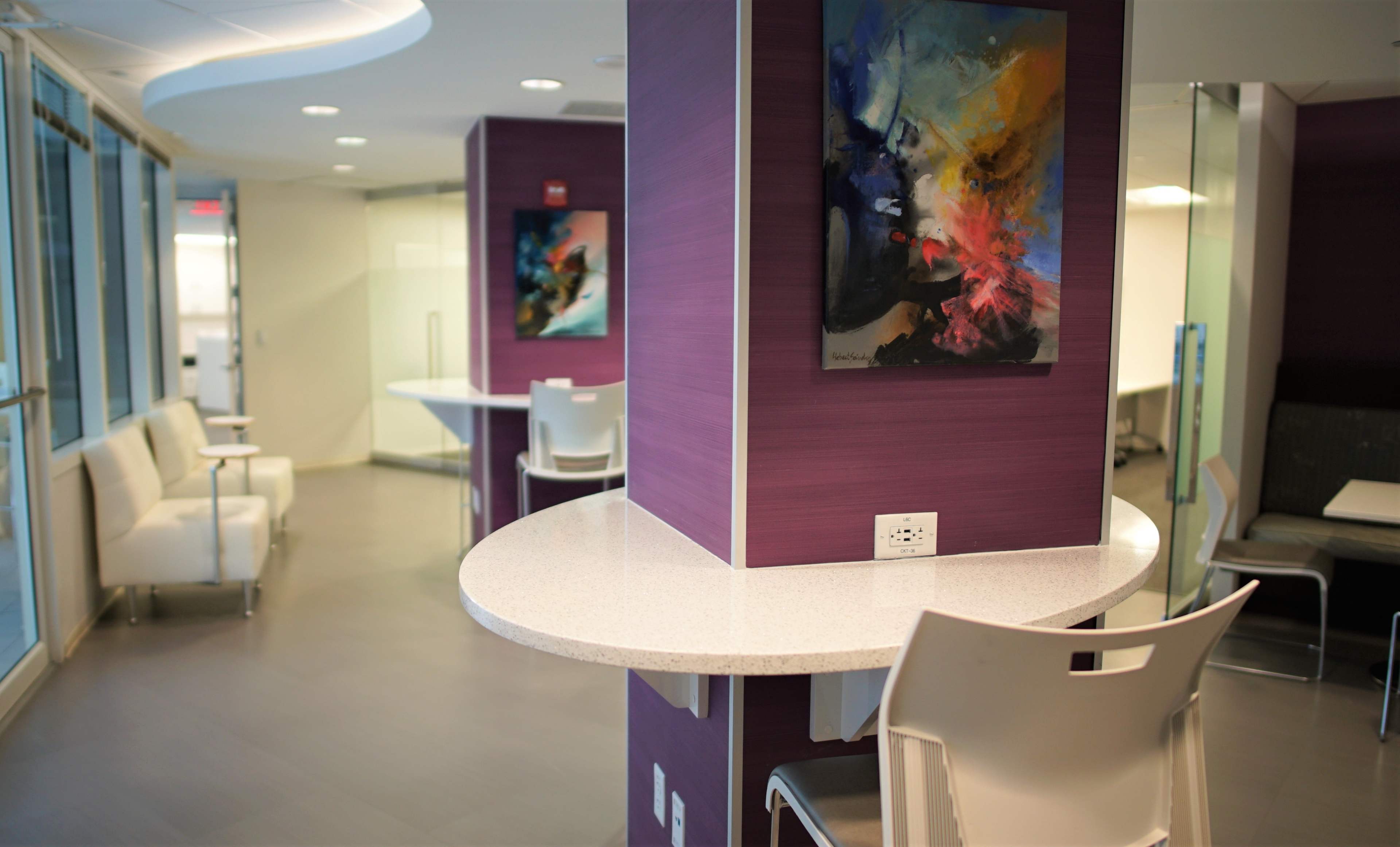 A modern, minimalist interior space with purple walls, circular tables, and contemporary art on display.
