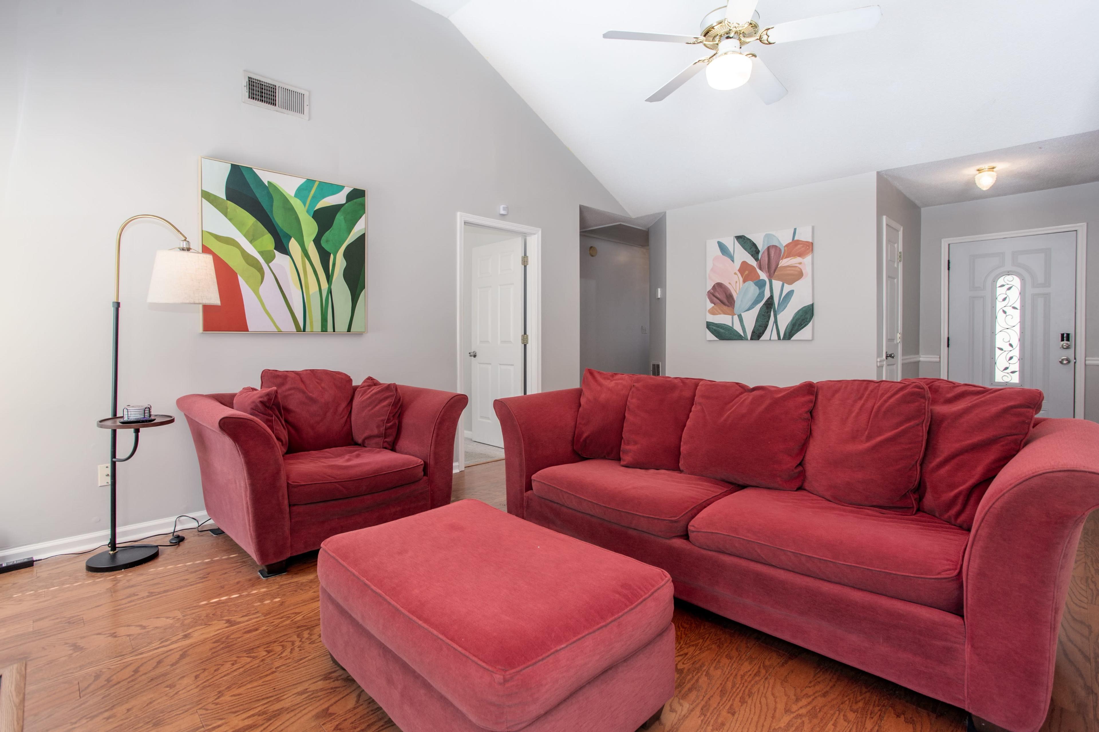 The living room features a red sofa, matching armchair, and an ottoman, accented by colorful wall art and a ceiling fan.