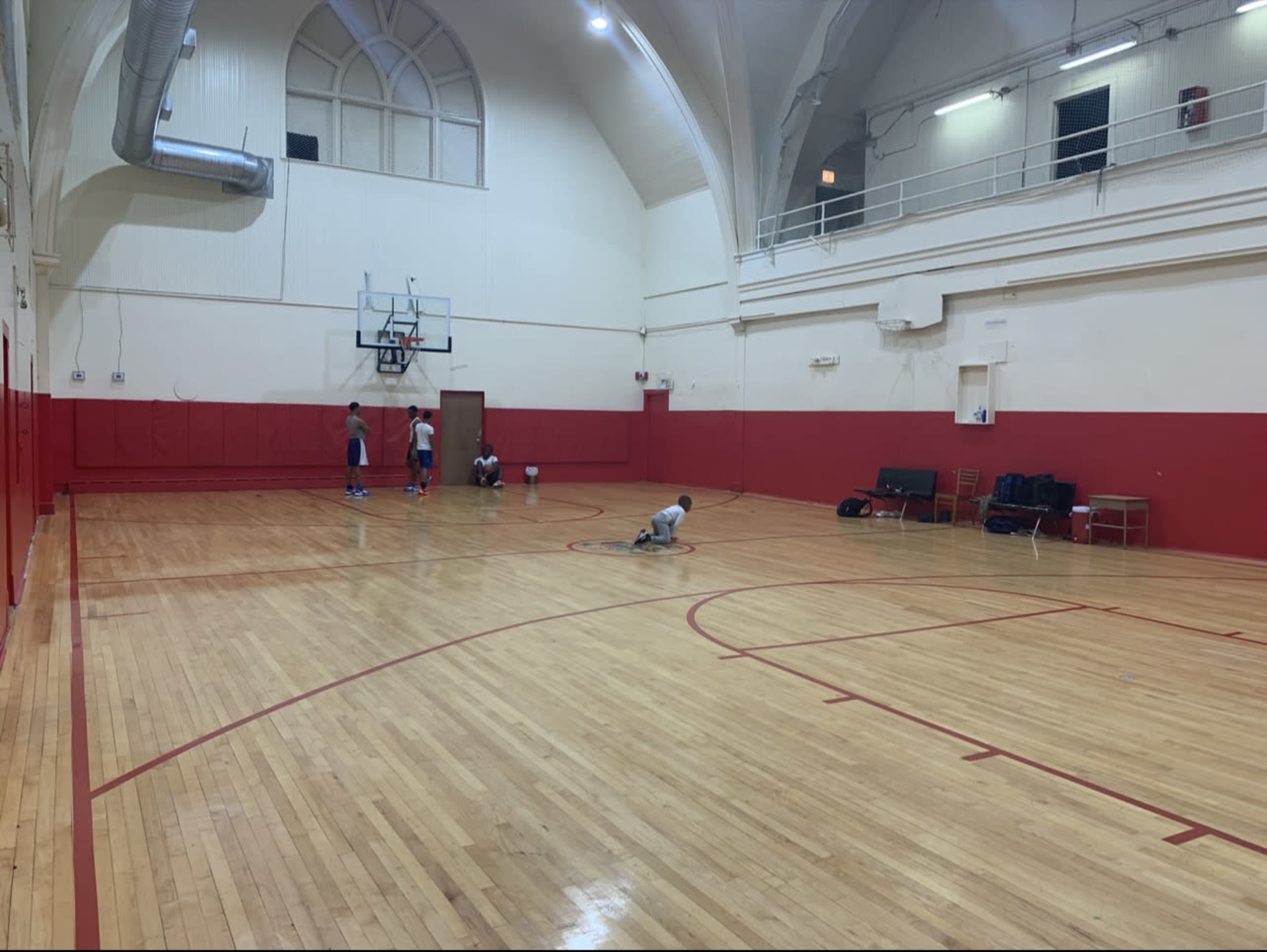 A group of individuals is practicing basketball on a wooden court inside a gymnasium with red walls.