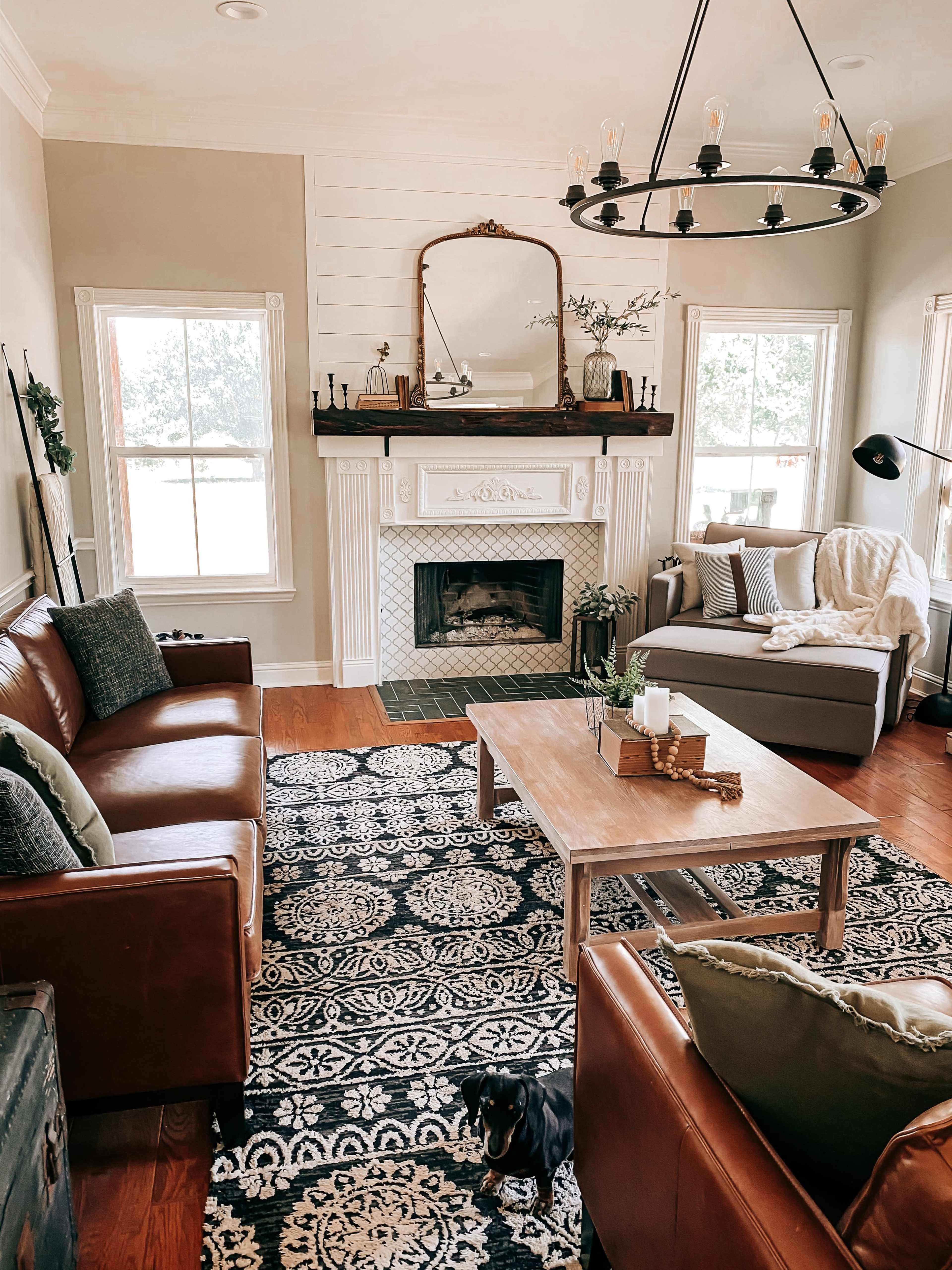 A cozy living room featuring two brown leather sofas, a wooden coffee table, and a fireplace with a decorative mirror above it, all set against a patterned rug.