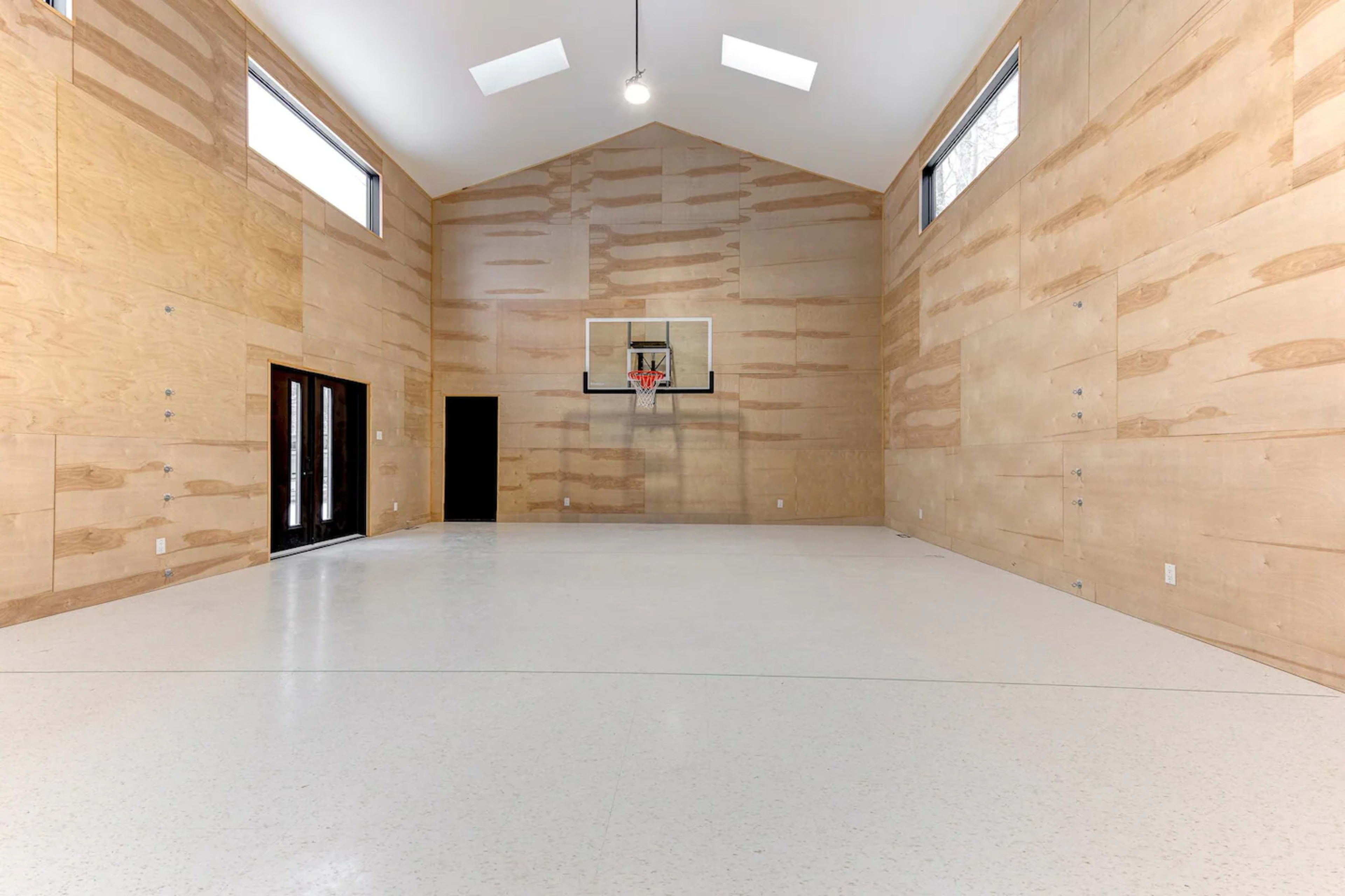 An indoor basketball court with wooden walls and a basketball hoop mounted at one end.