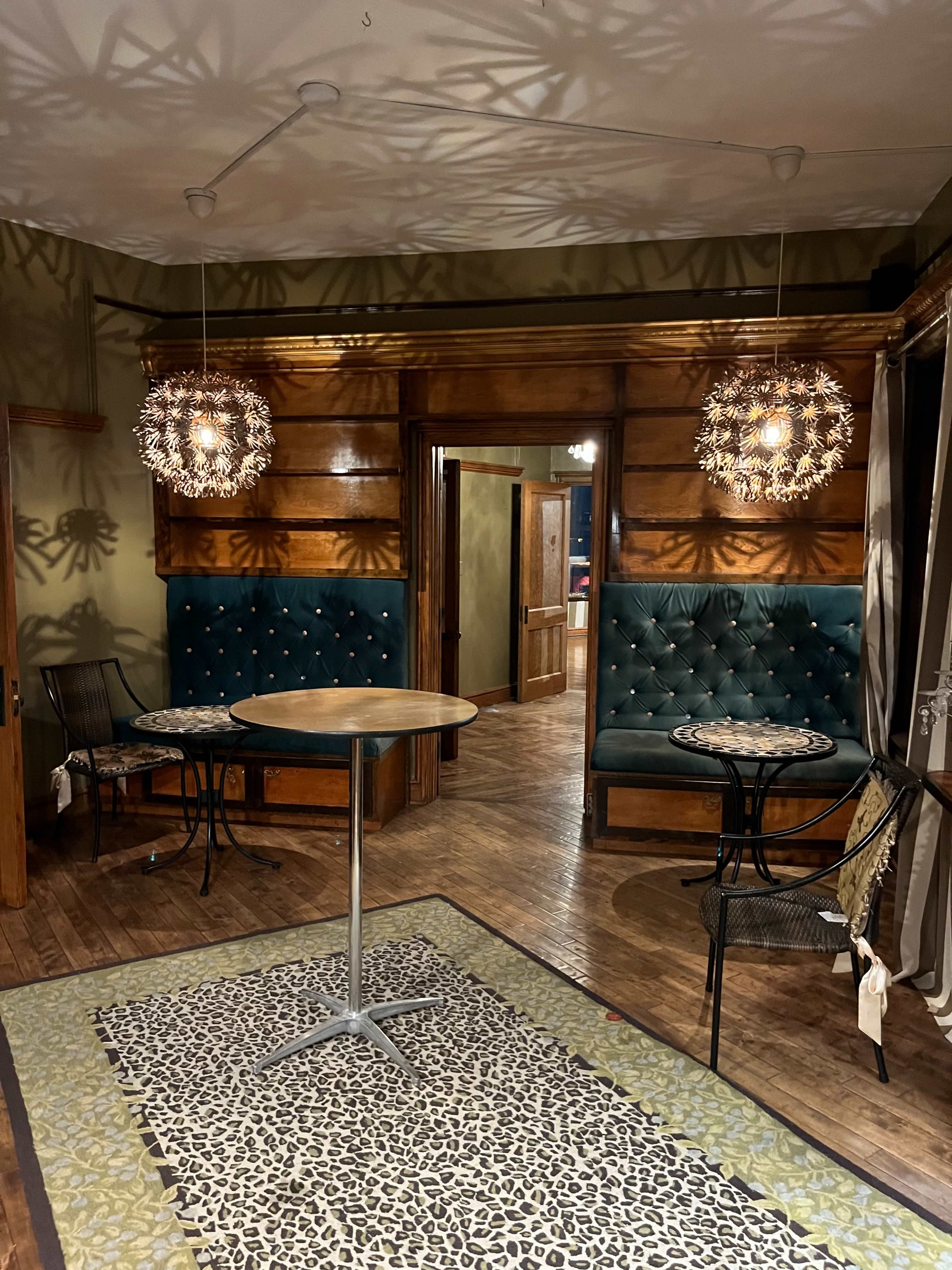 A cozy interior space featuring two pendant lights, a small round table, and teal upholstered seating along wooden walls, with a patterned rug on the floor.