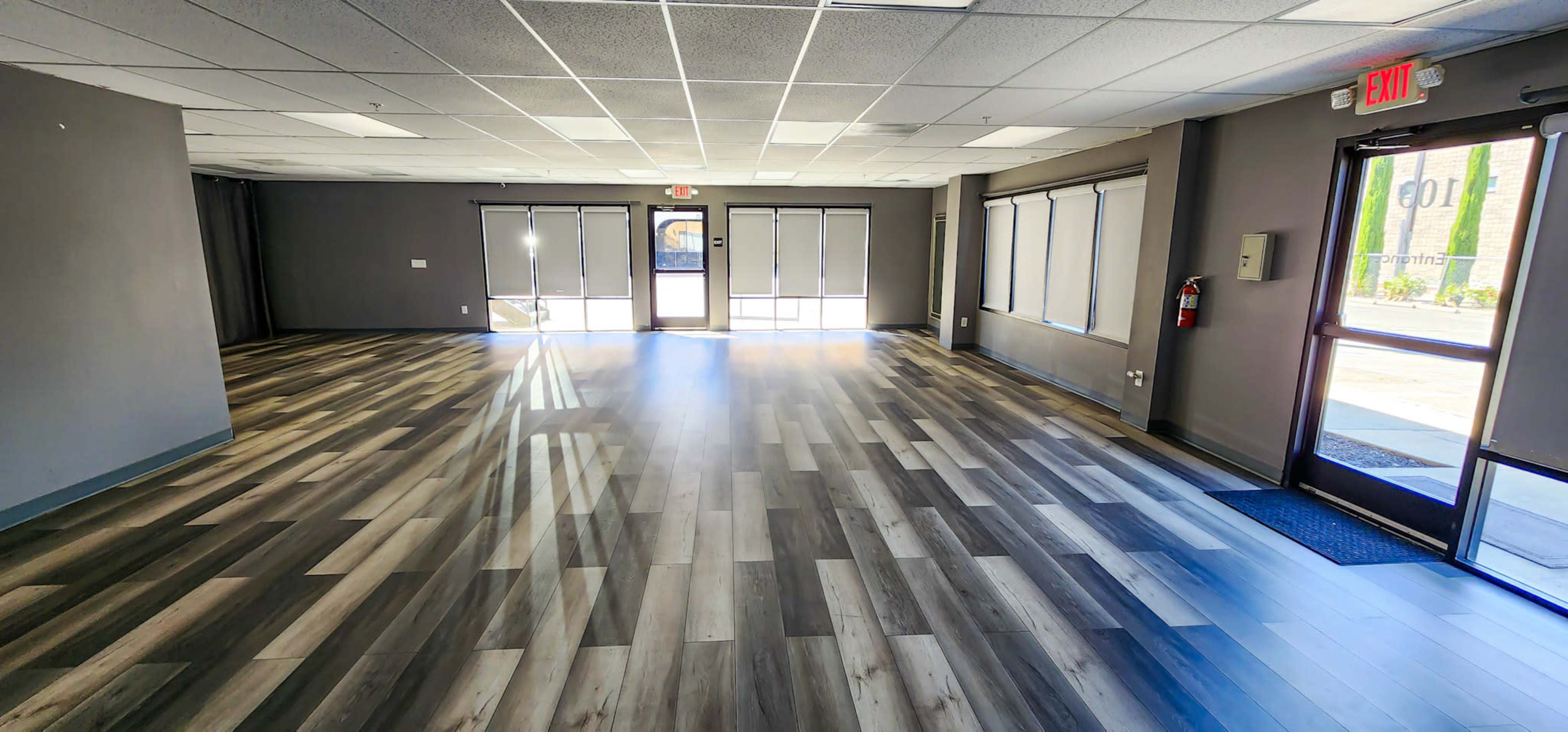An empty commercial space with gray laminate flooring and large windows letting in natural light.