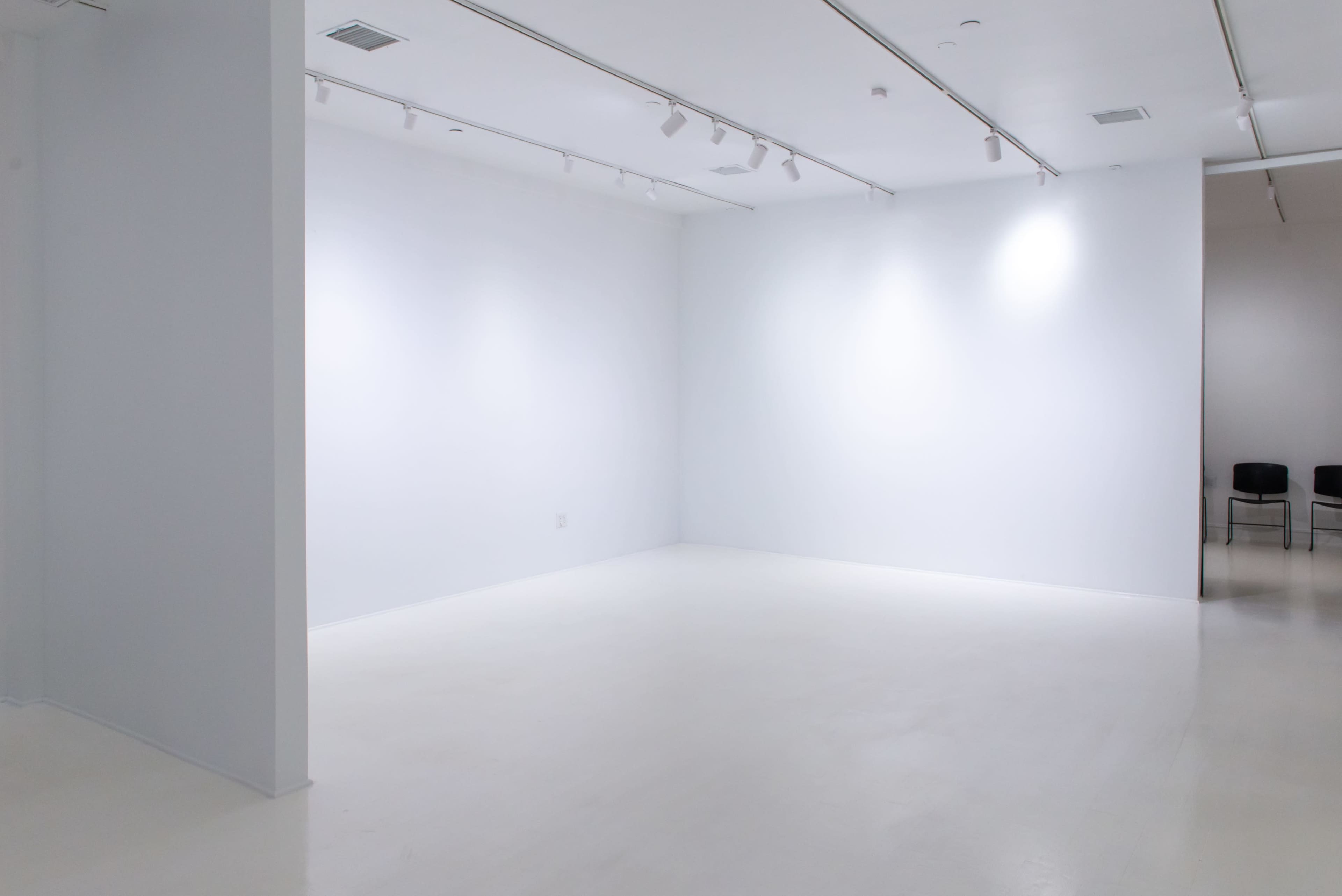 A large, empty, well-lit gallery space with white walls and a polished floor.