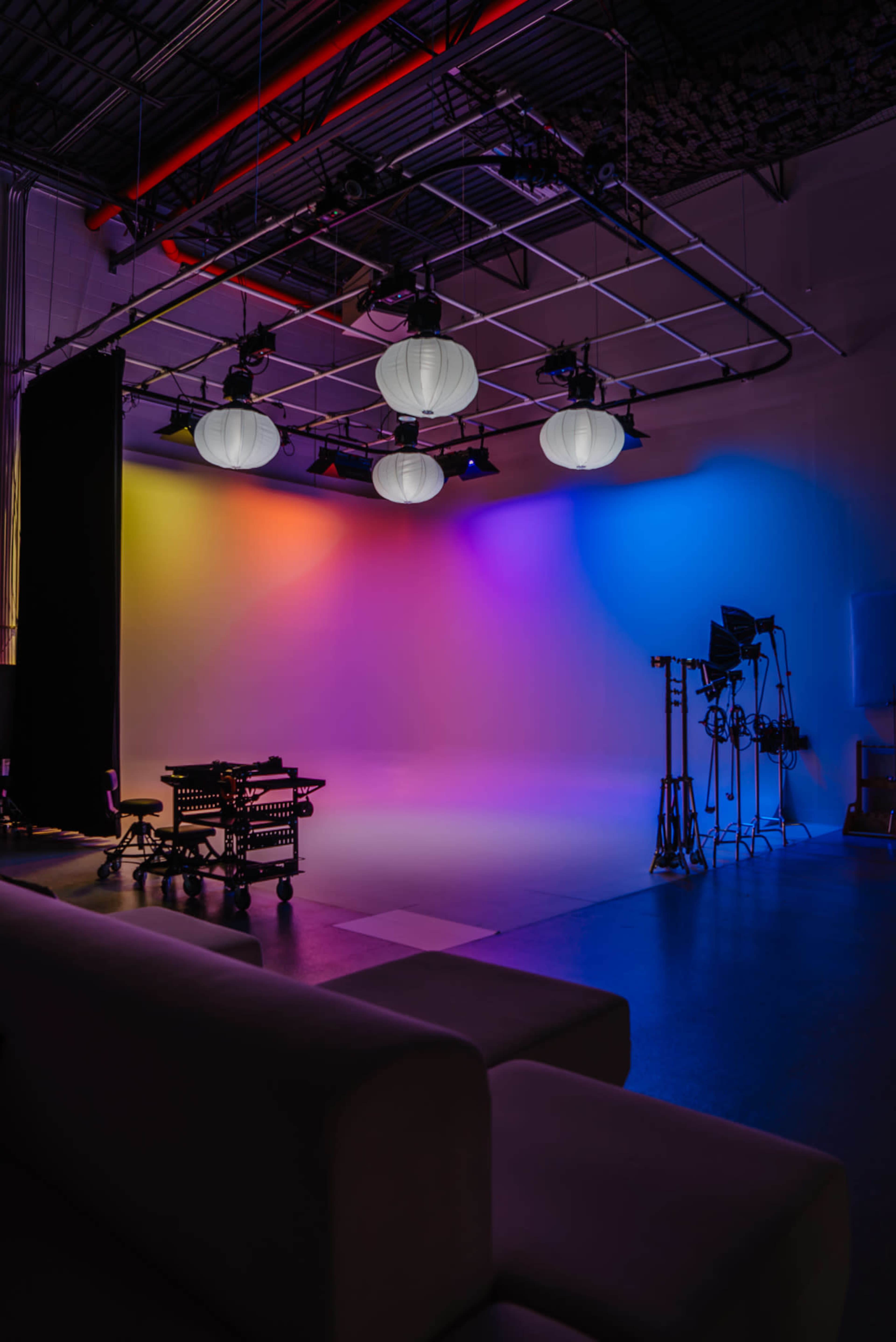 The image shows a photography studio with colorful lighting, suspended lanterns, and equipment in the background.