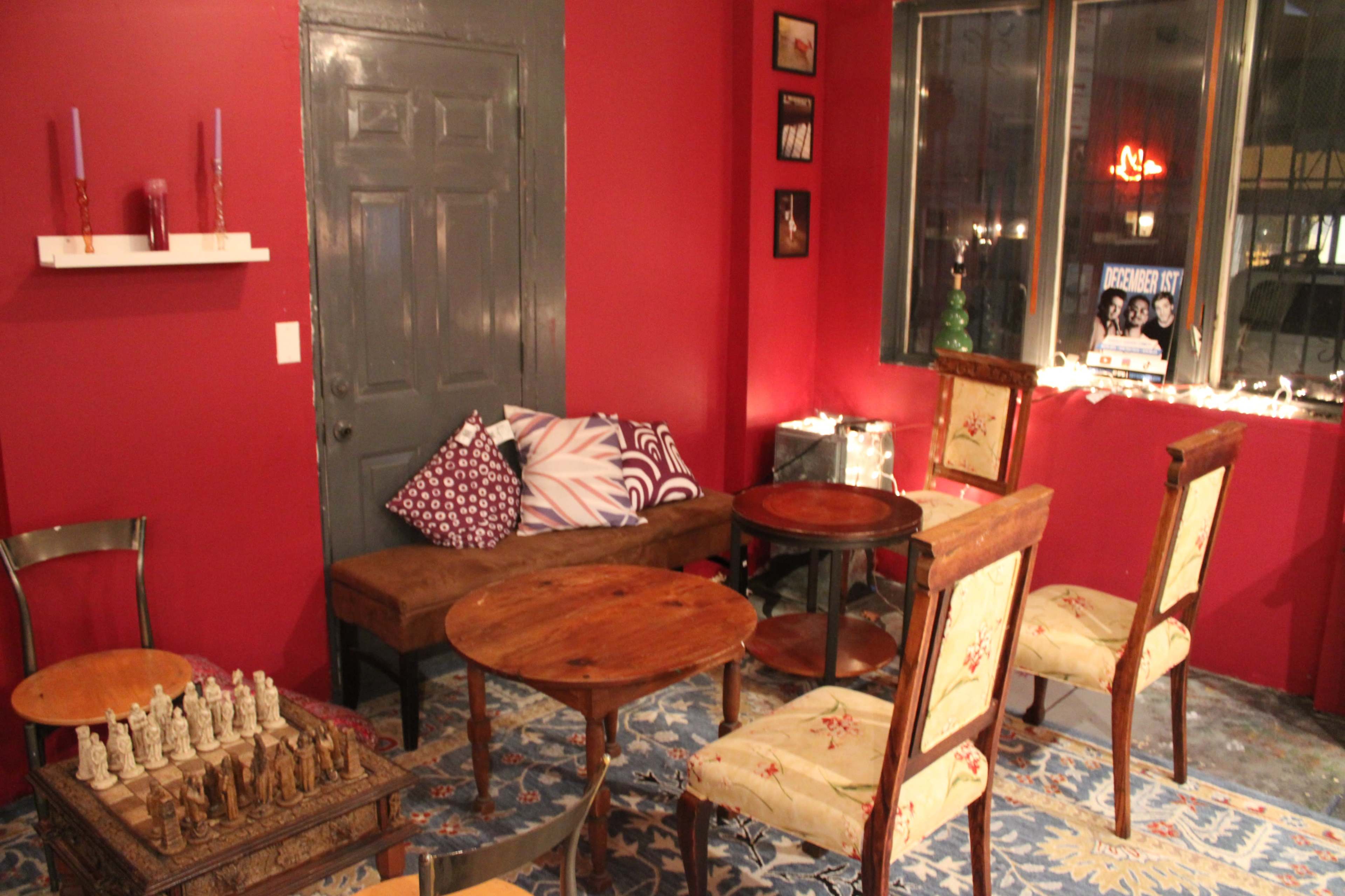 A cozy room with red walls, wooden tables, a chess set, and seating arranged around a window.