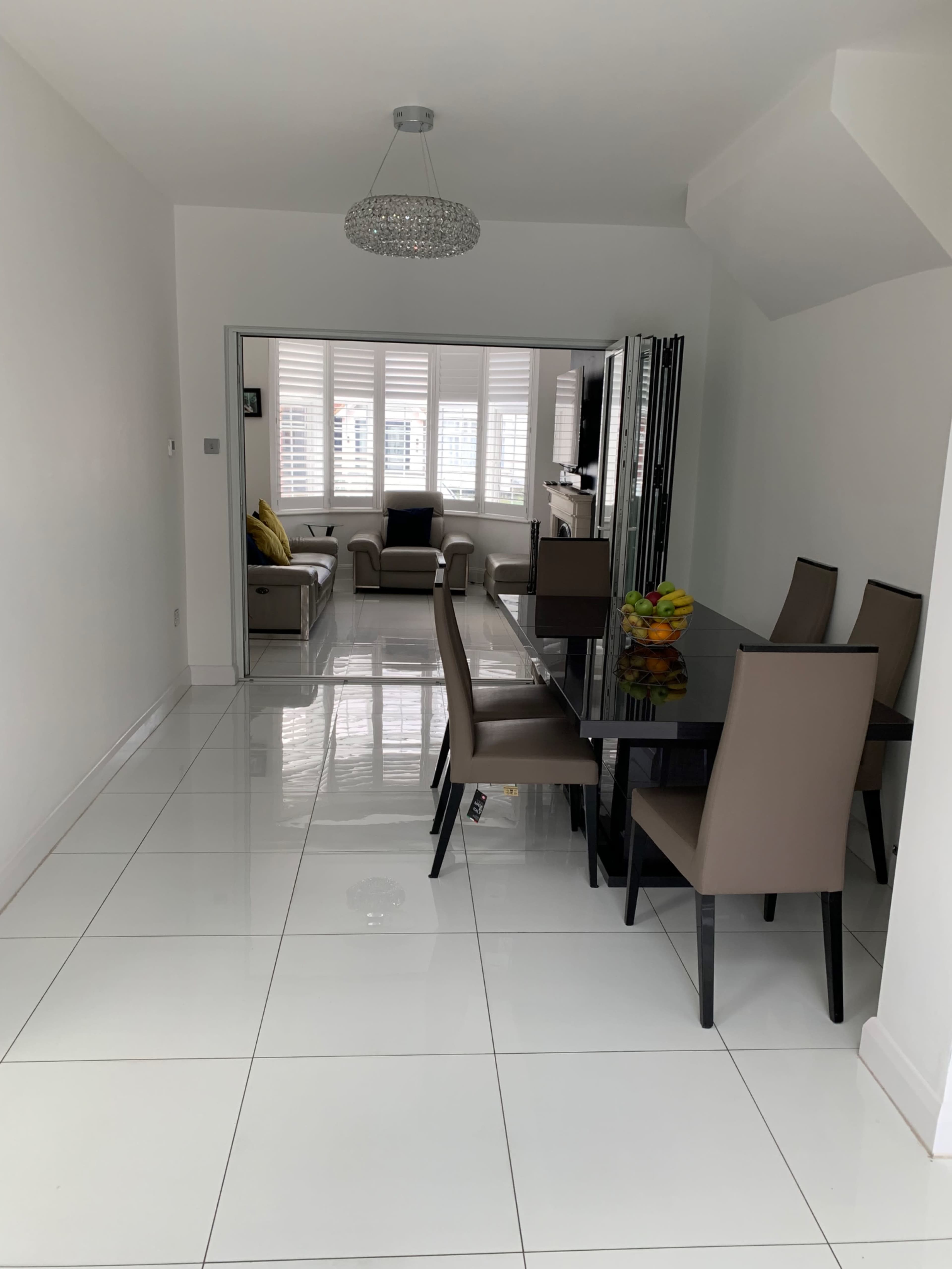 A modern dining area with a glass table and six chairs, leading into a bright living space with a sofa and large windows.