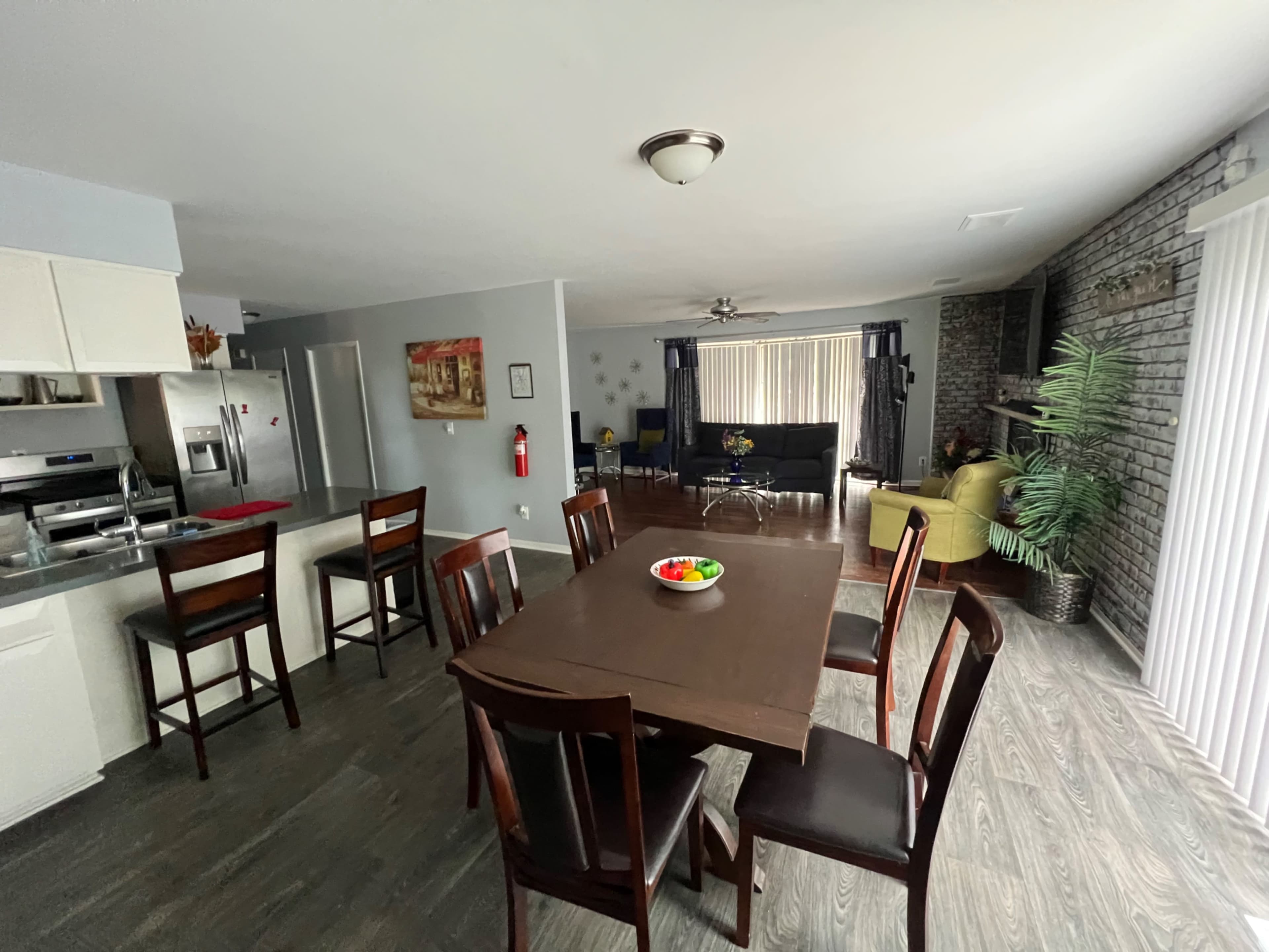 A dining area with a rectangular table and eight chairs is visible, leading to a living space with a black couch and a green chair.