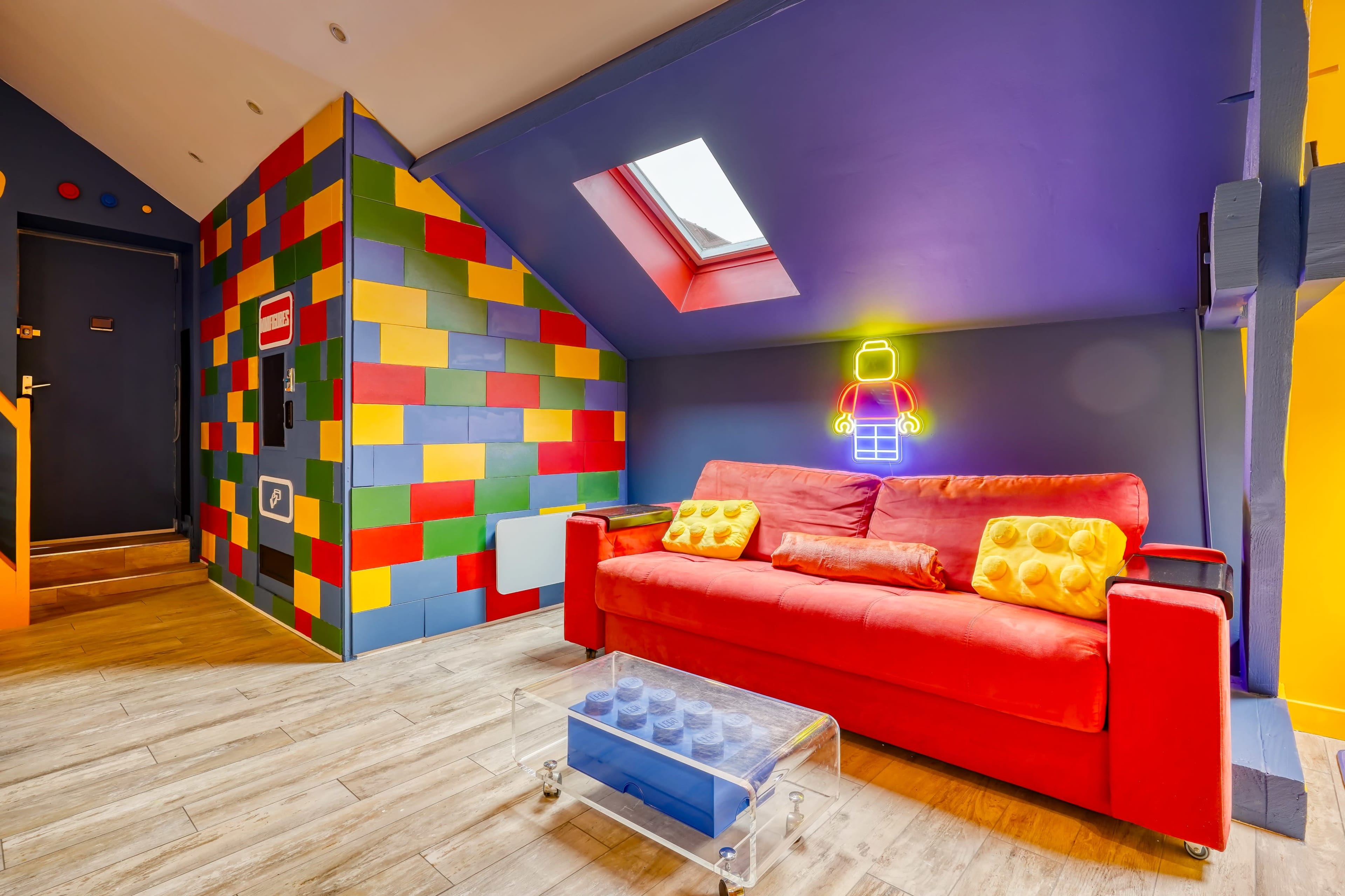 The image shows a colorful room with a red couch, a clear coffee table, and a wall decorated with bright, multi-colored blocks.