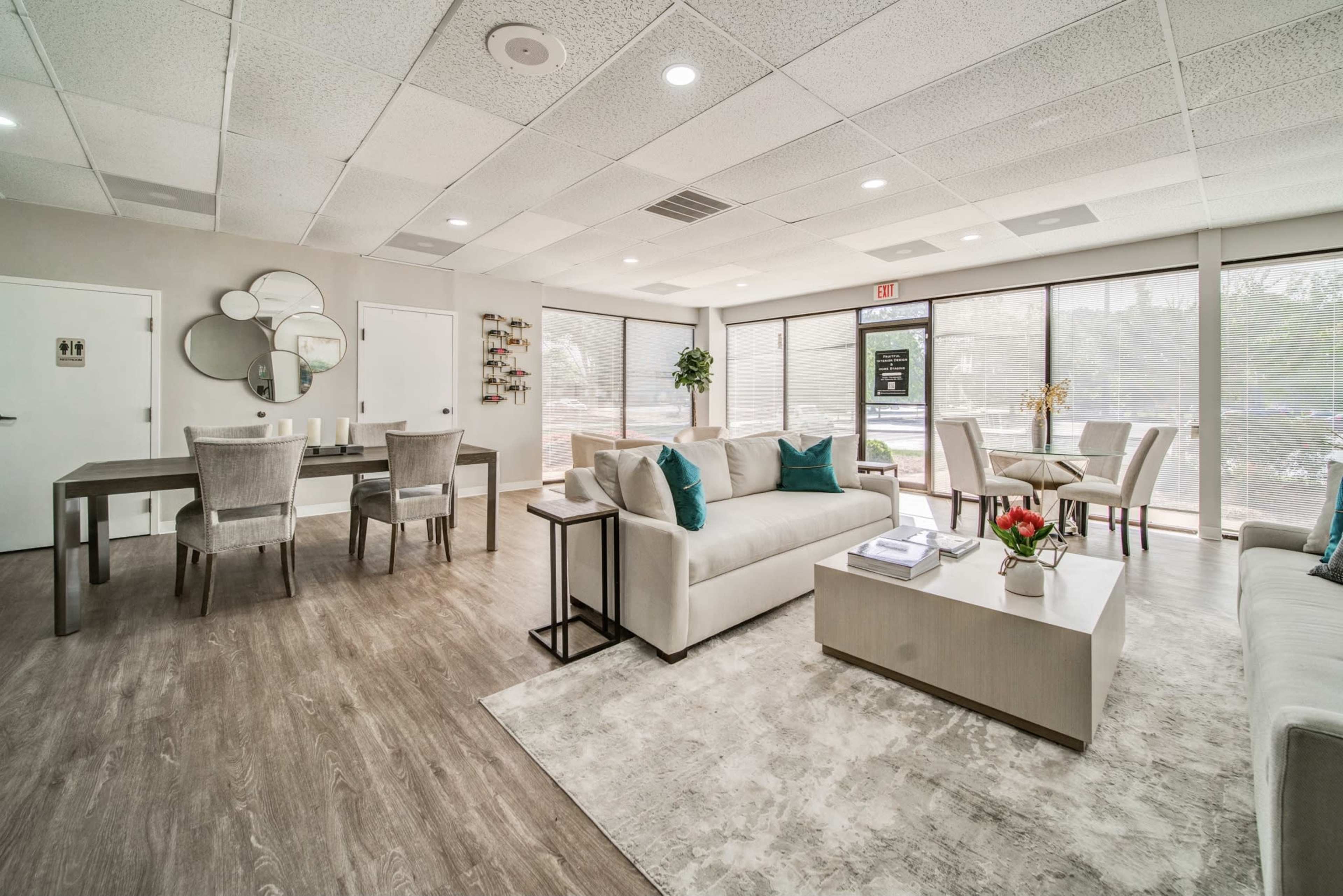 A modern lounge area features a seating arrangement with light-colored sofas, a coffee table, and a dining table alongside large windows letting in natural light.