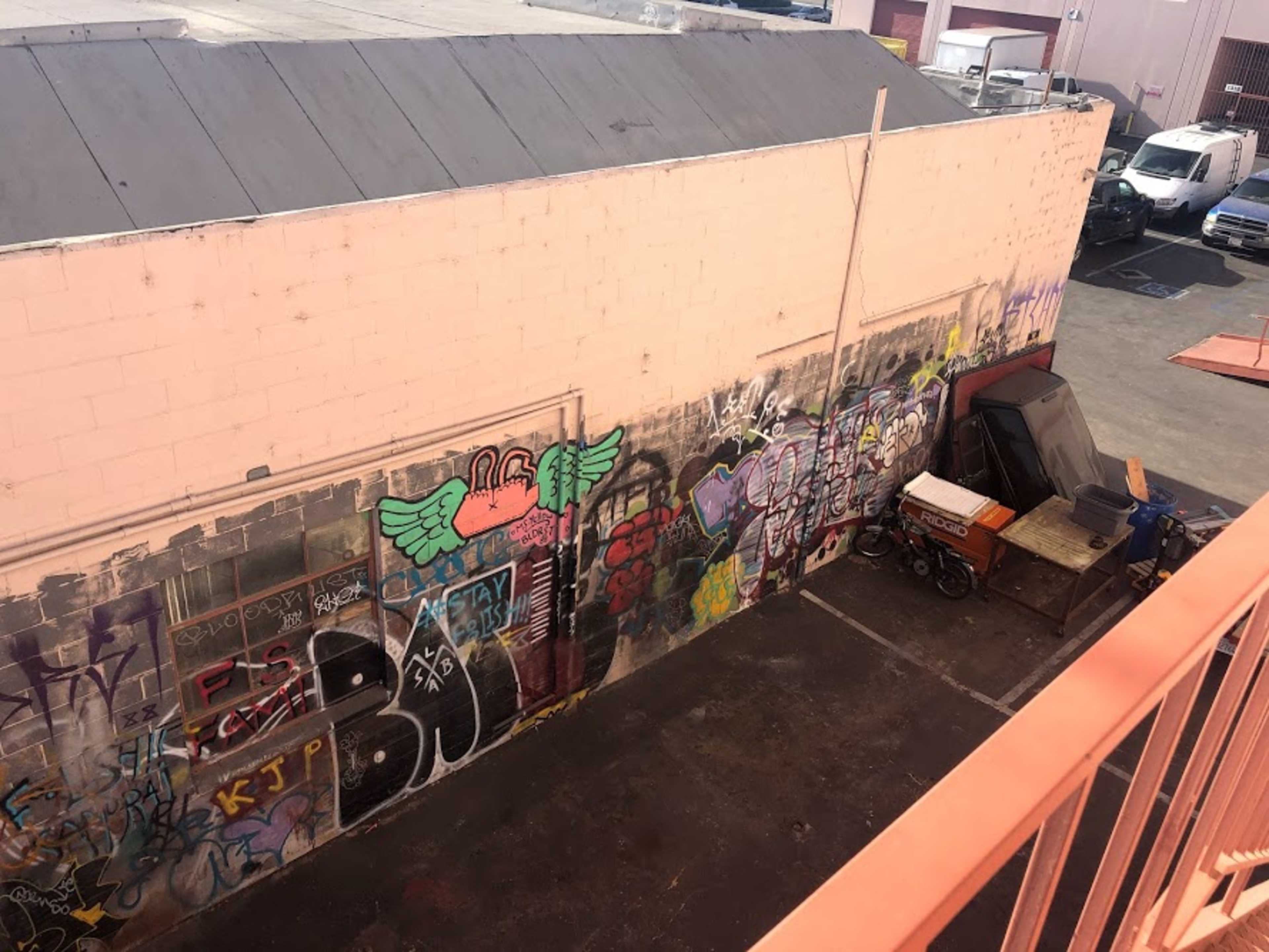 A brightly painted wall covered in graffiti, positioned next to a cluttered area with industrial items and vehicles.