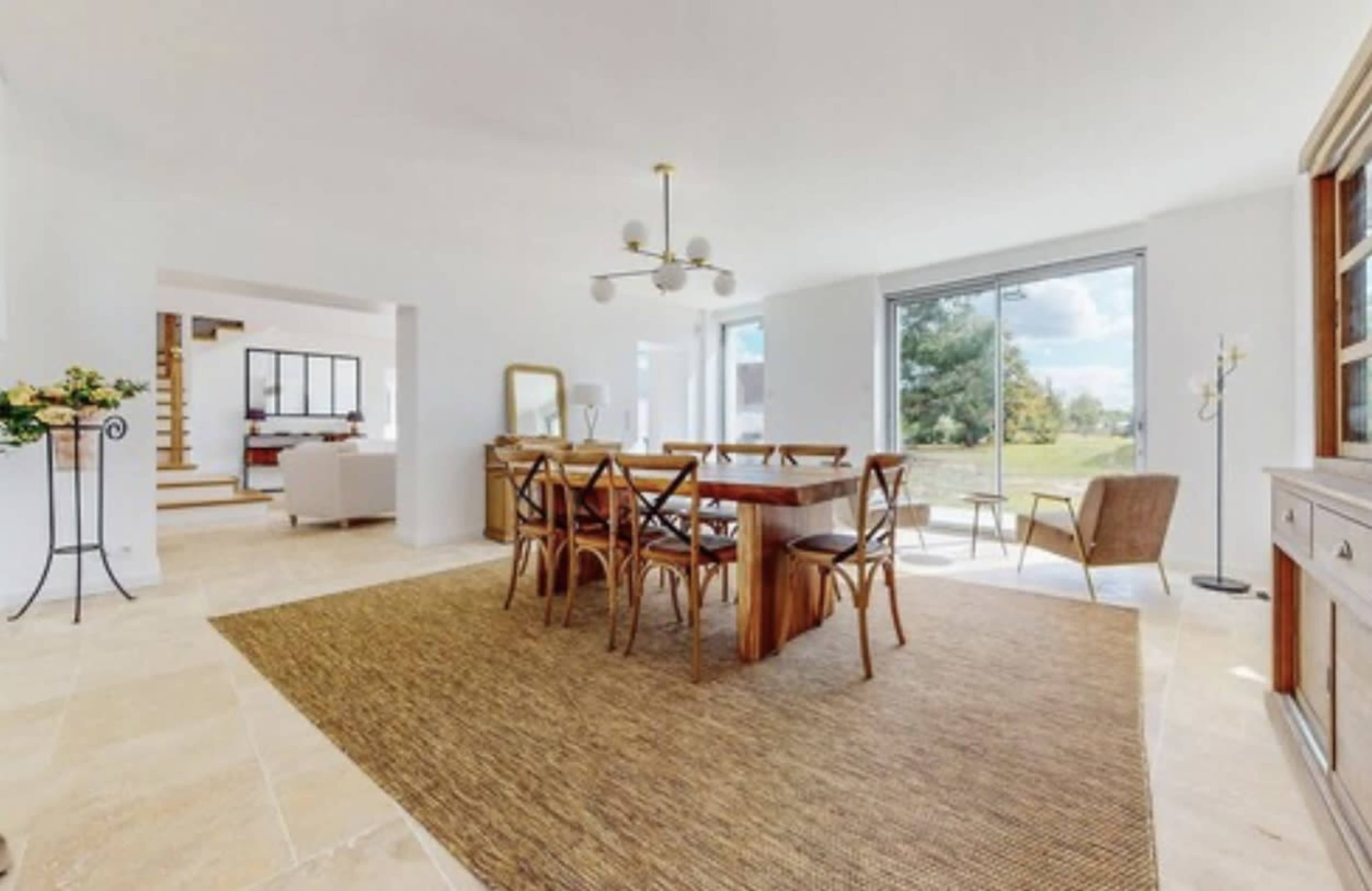 A spacious dining area features a wooden table surrounded by chairs, with large windows offering a view of the outdoors.