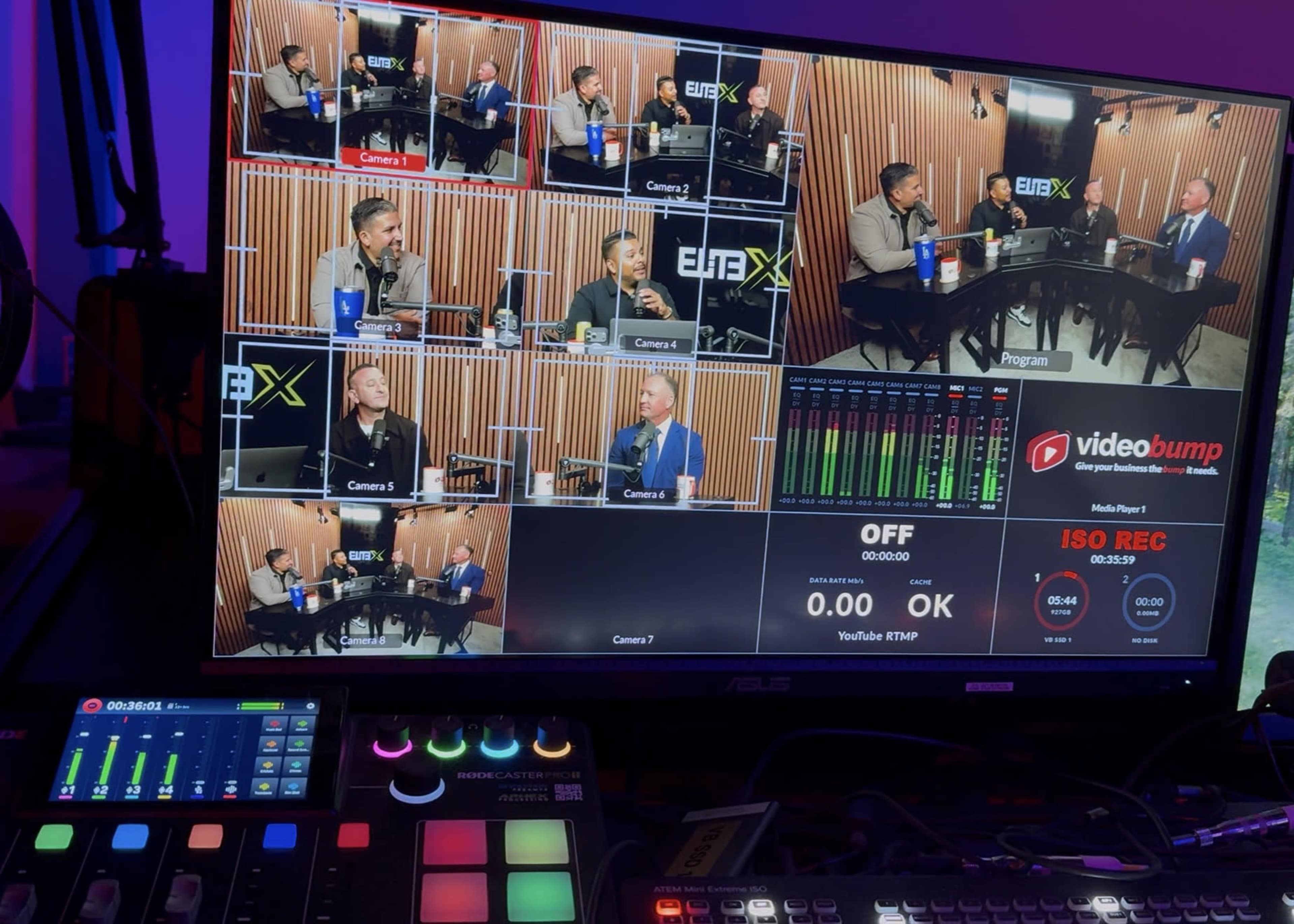 The image shows a video production setup displaying a multi-camera live stream with various participants engaged in a discussion at a table.