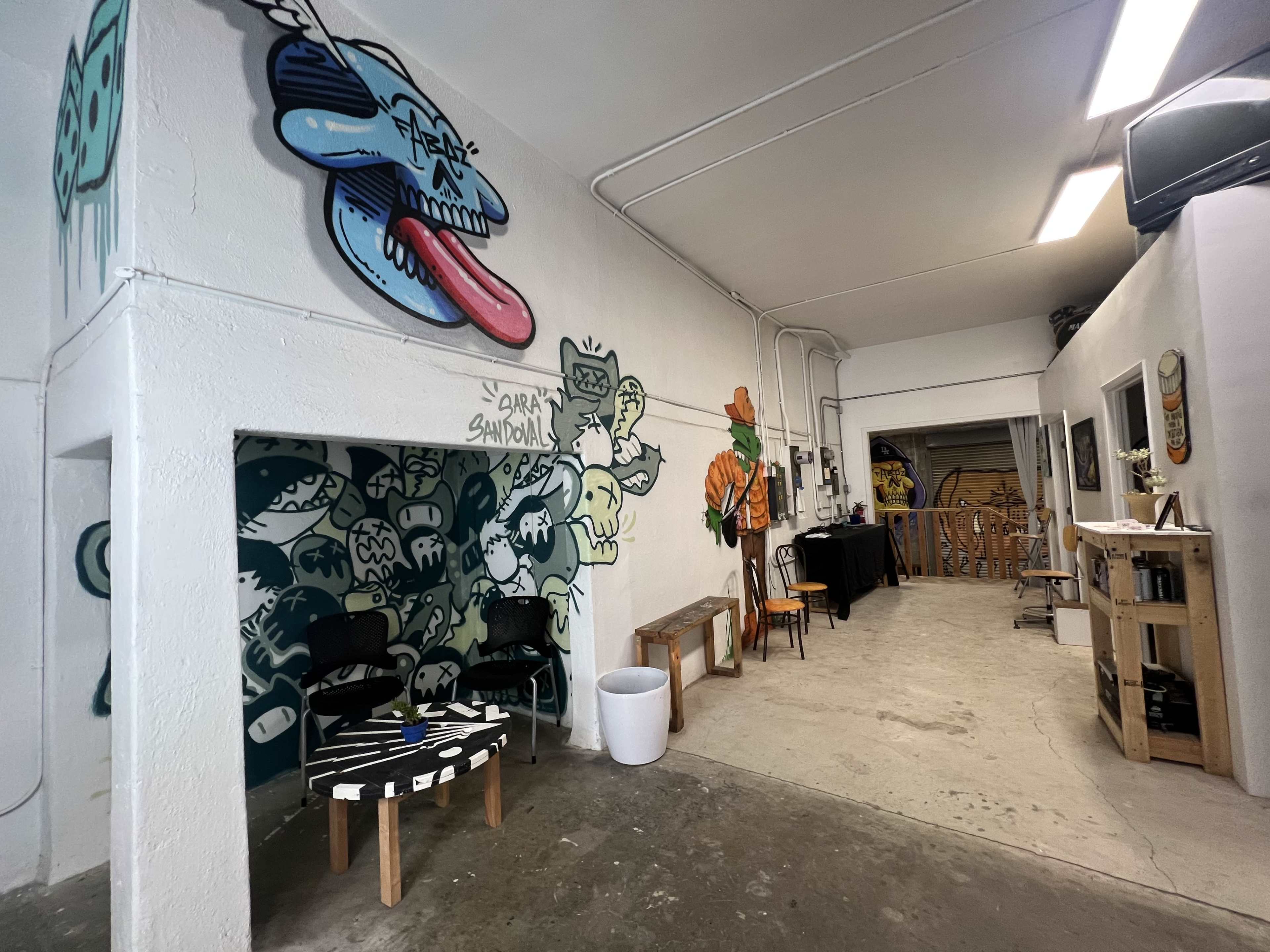 The image shows an industrial-style interior with graffiti-covered walls, featuring a seating area and a workspace in the background.