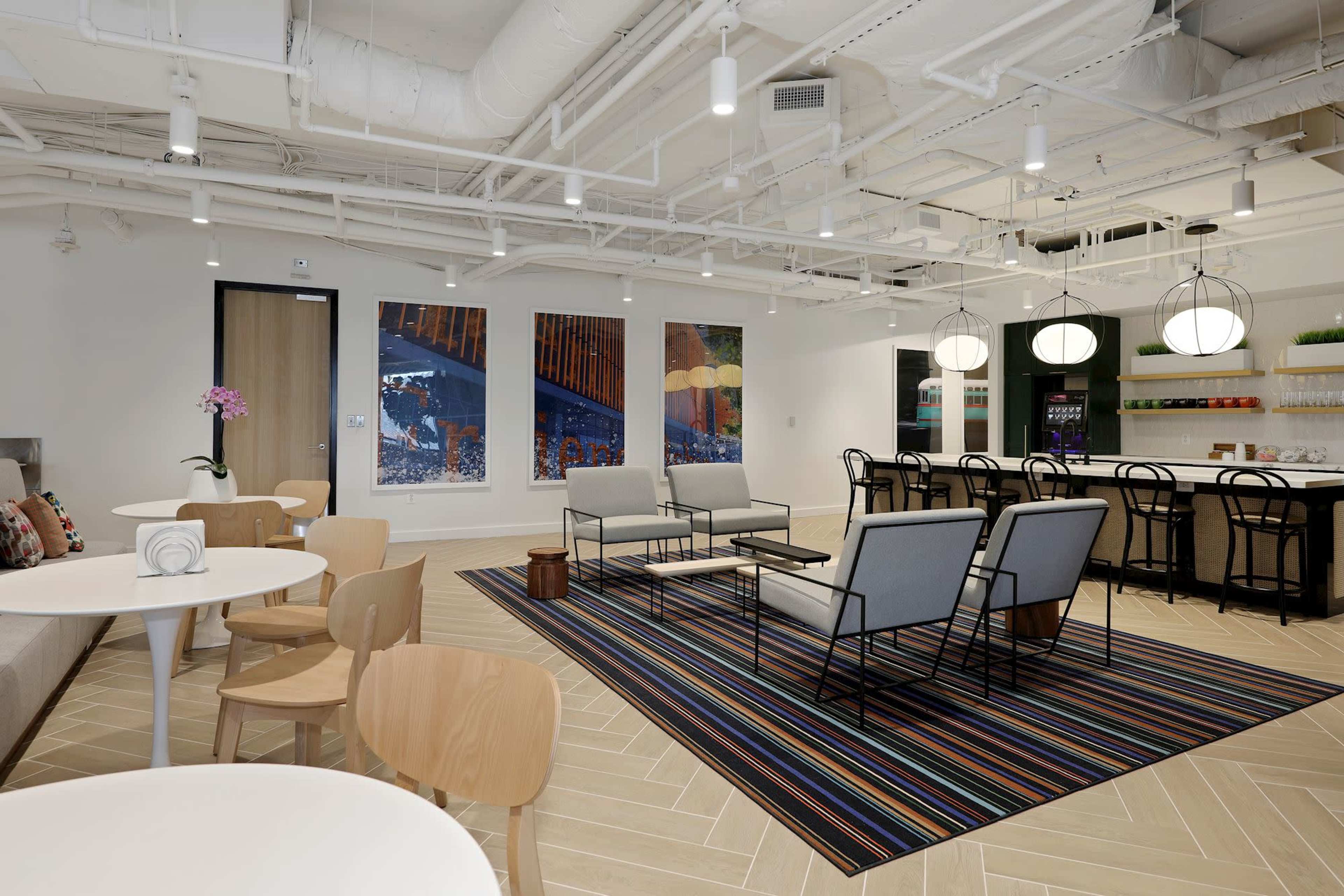 A modern communal space featuring seating areas, a dining area, and colorful artwork on the walls.