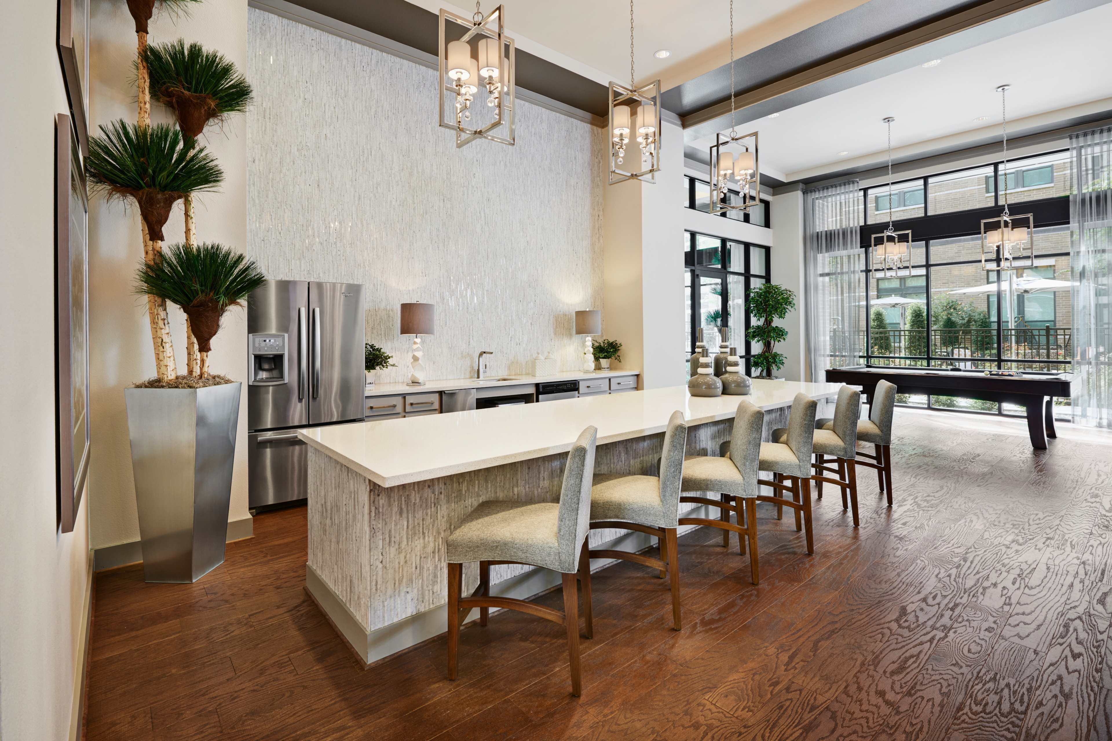 A modern kitchen area with a long countertop, several bar stools, and large windows that allow natural light to fill the space.