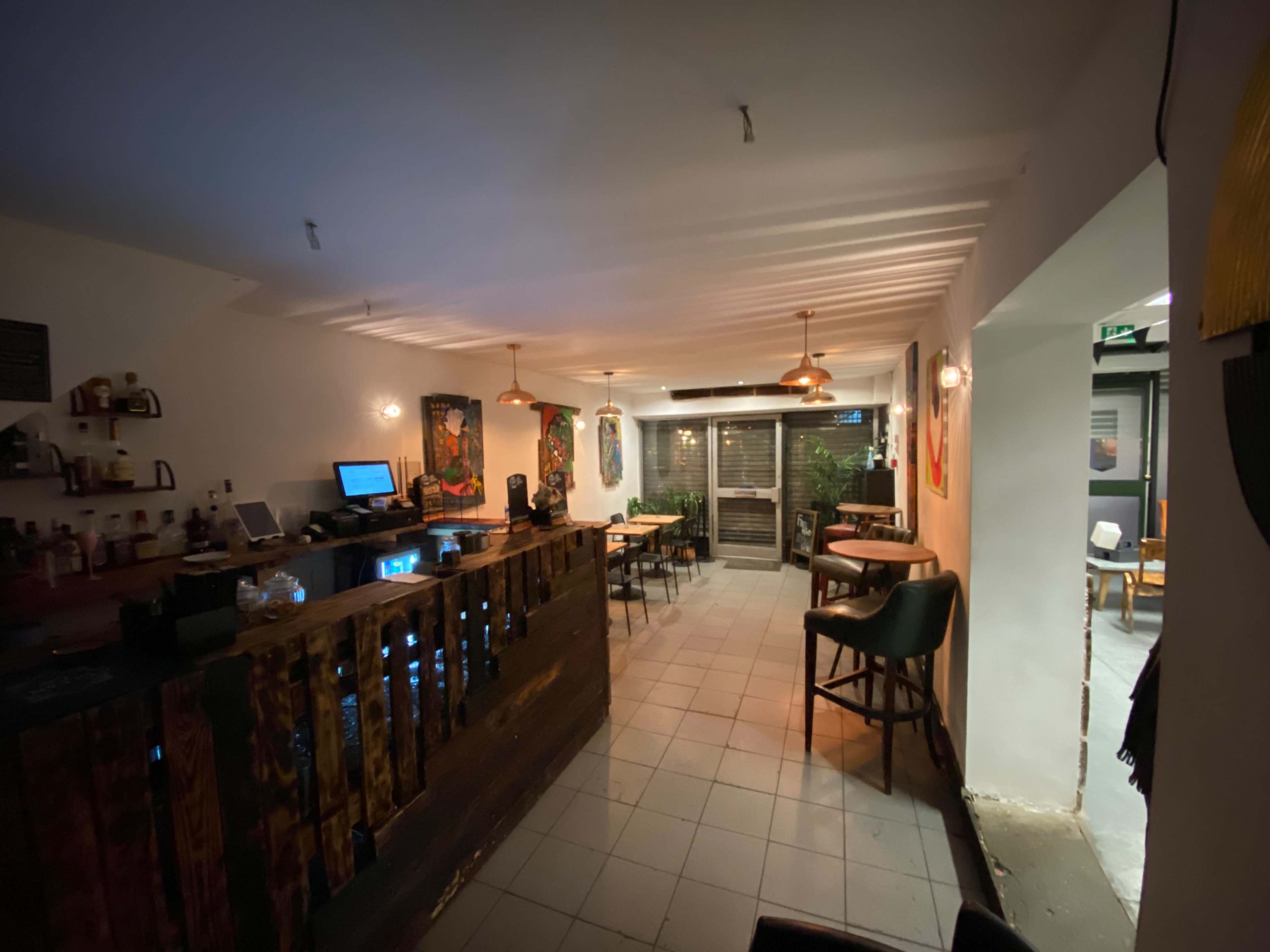 The image shows the interior of a restaurant or bar featuring a wooden counter, seating areas, and ambient lighting.