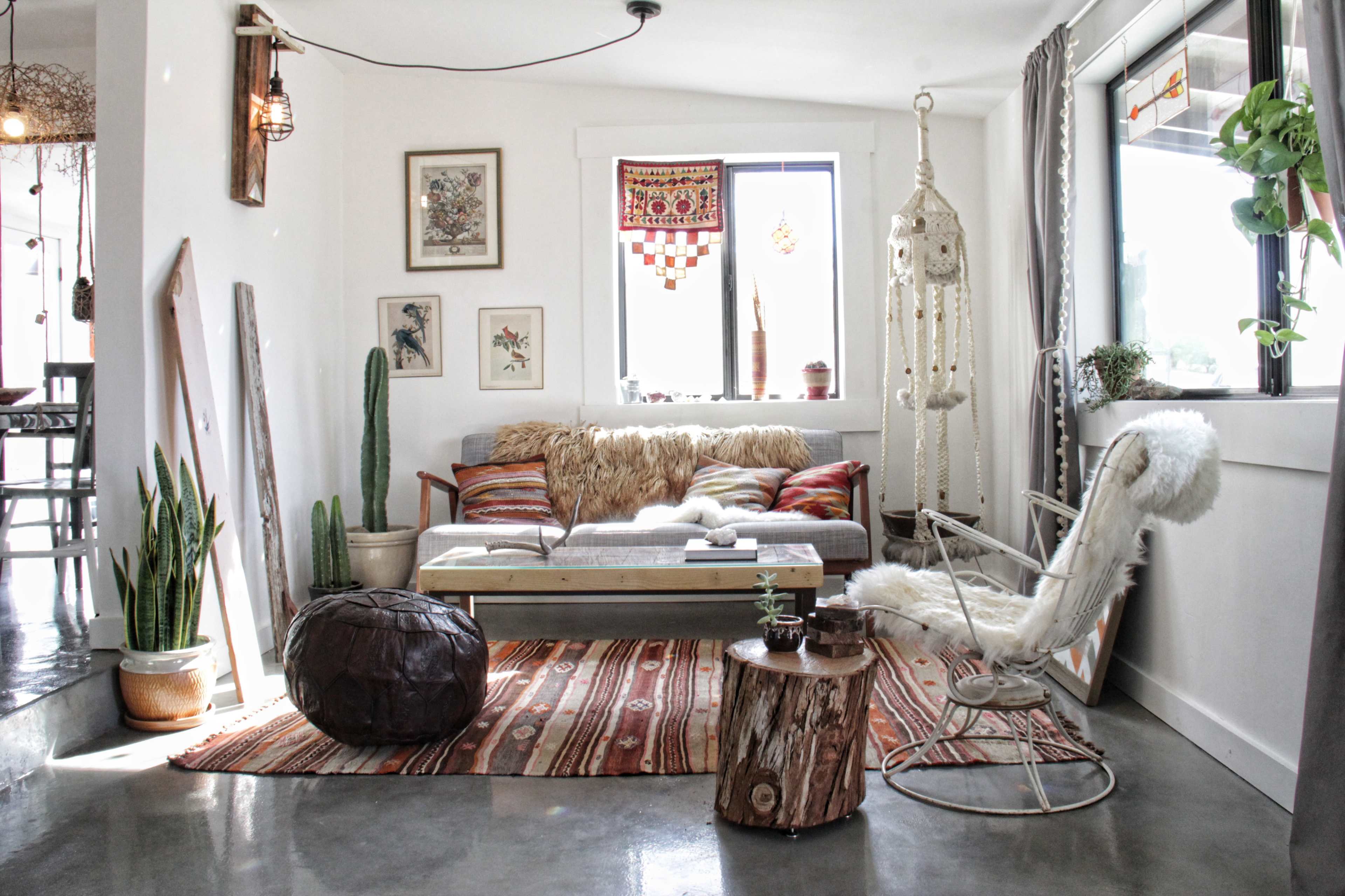 A cozy living room with a mid-century style couch, a macramé hanging chair, potted plants, and colorful rugs.