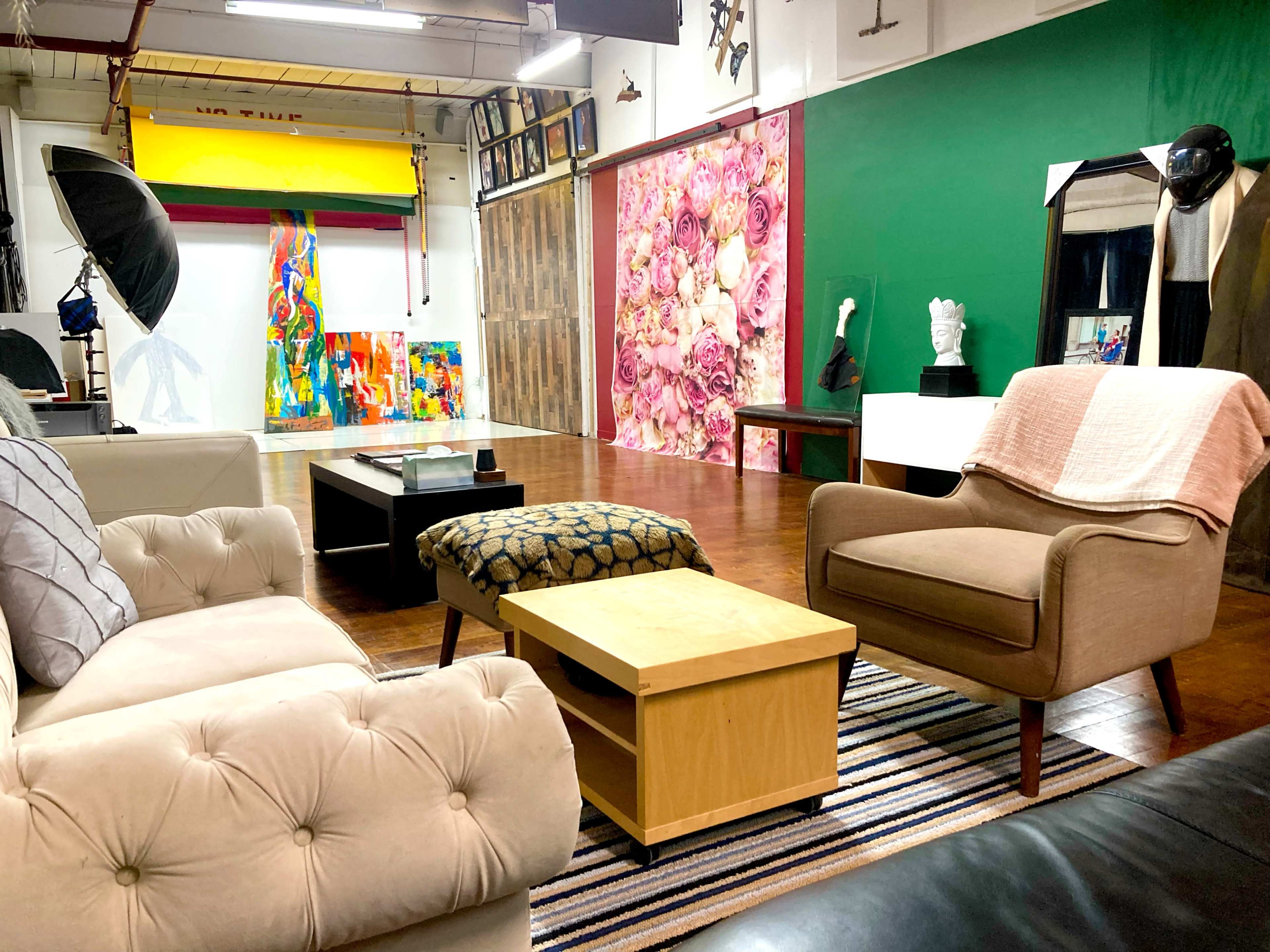 A spacious art studio featuring various colorful artworks, different seating arrangements, and a backdrop with a floral design.