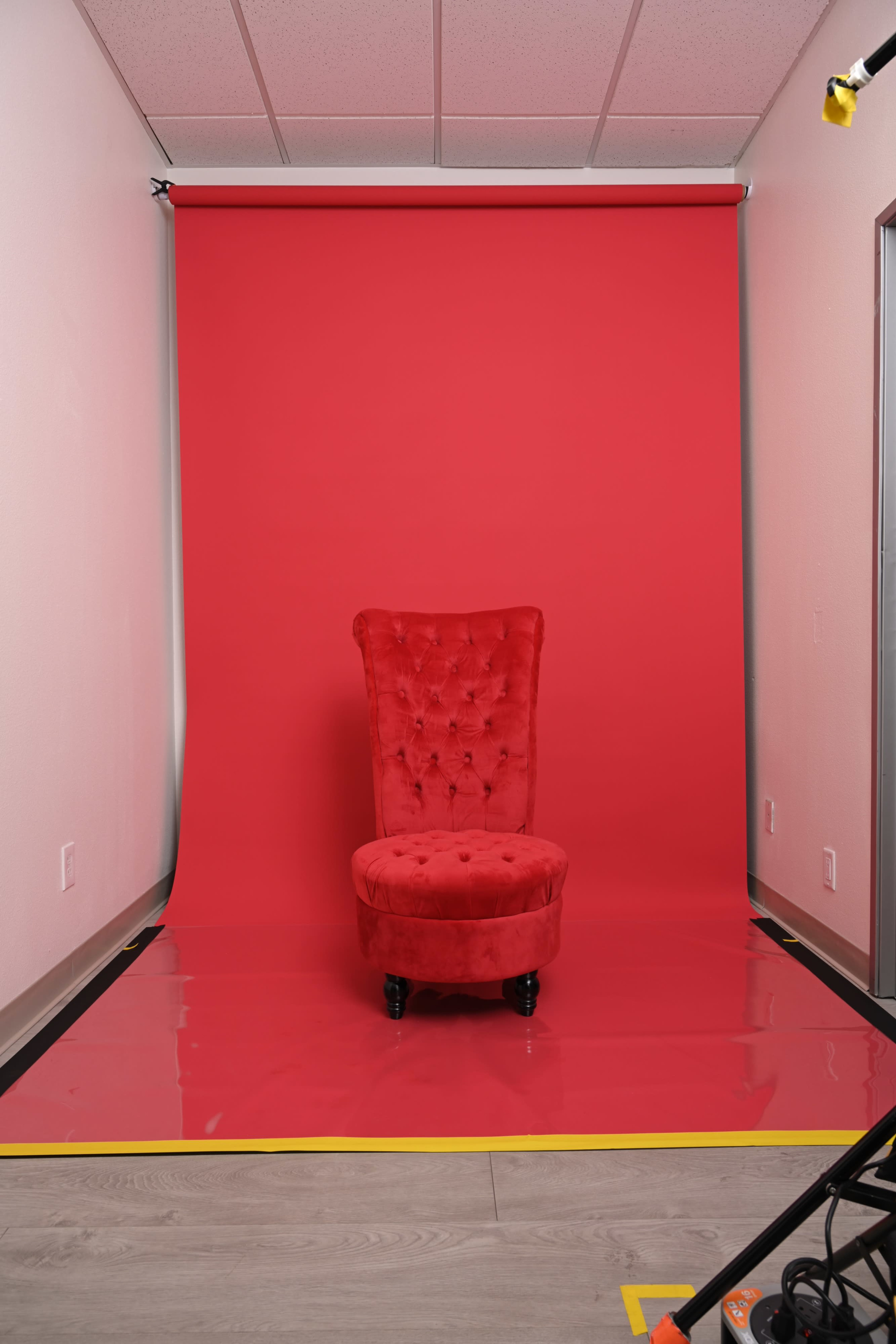 A red upholstered chair is positioned against a solid red background in a well-lit studio space.