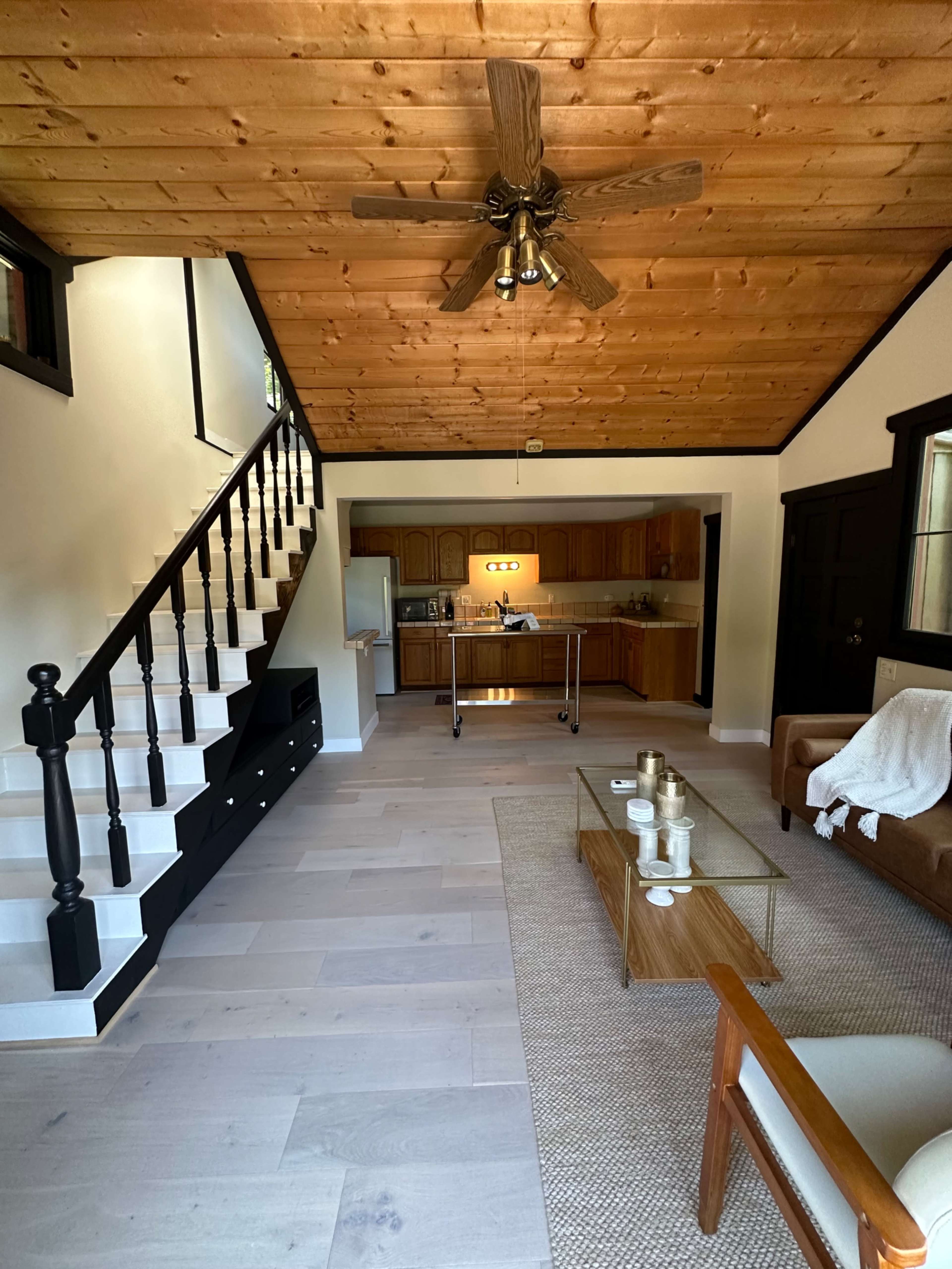 A wooden interior living space featuring a staircase, a kitchen area, and a seating arrangement with a coffee table.