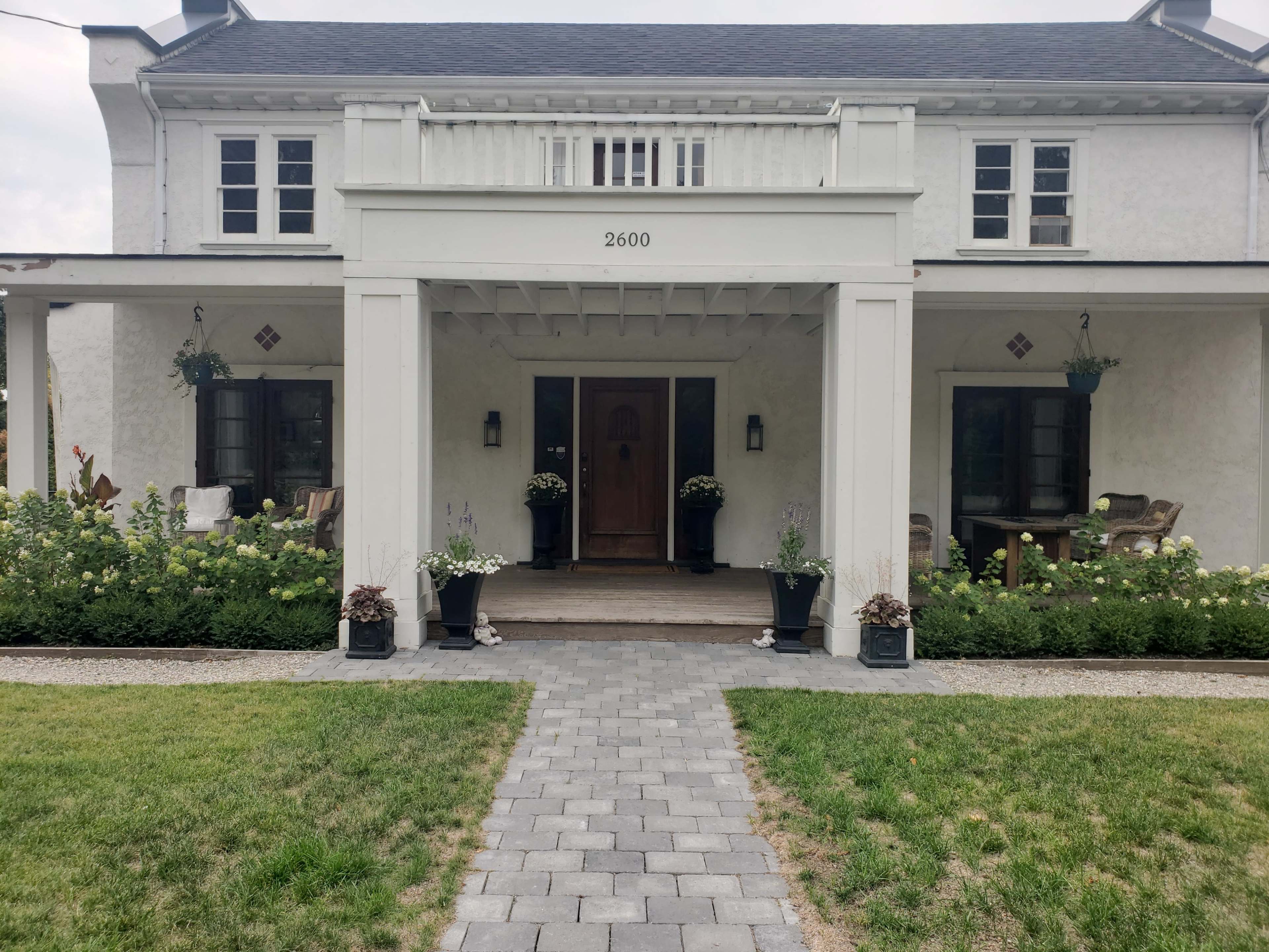 A white, two-story house with a central front porch and a stone pathway leading to the entrance, surrounded by well-maintained flower beds.