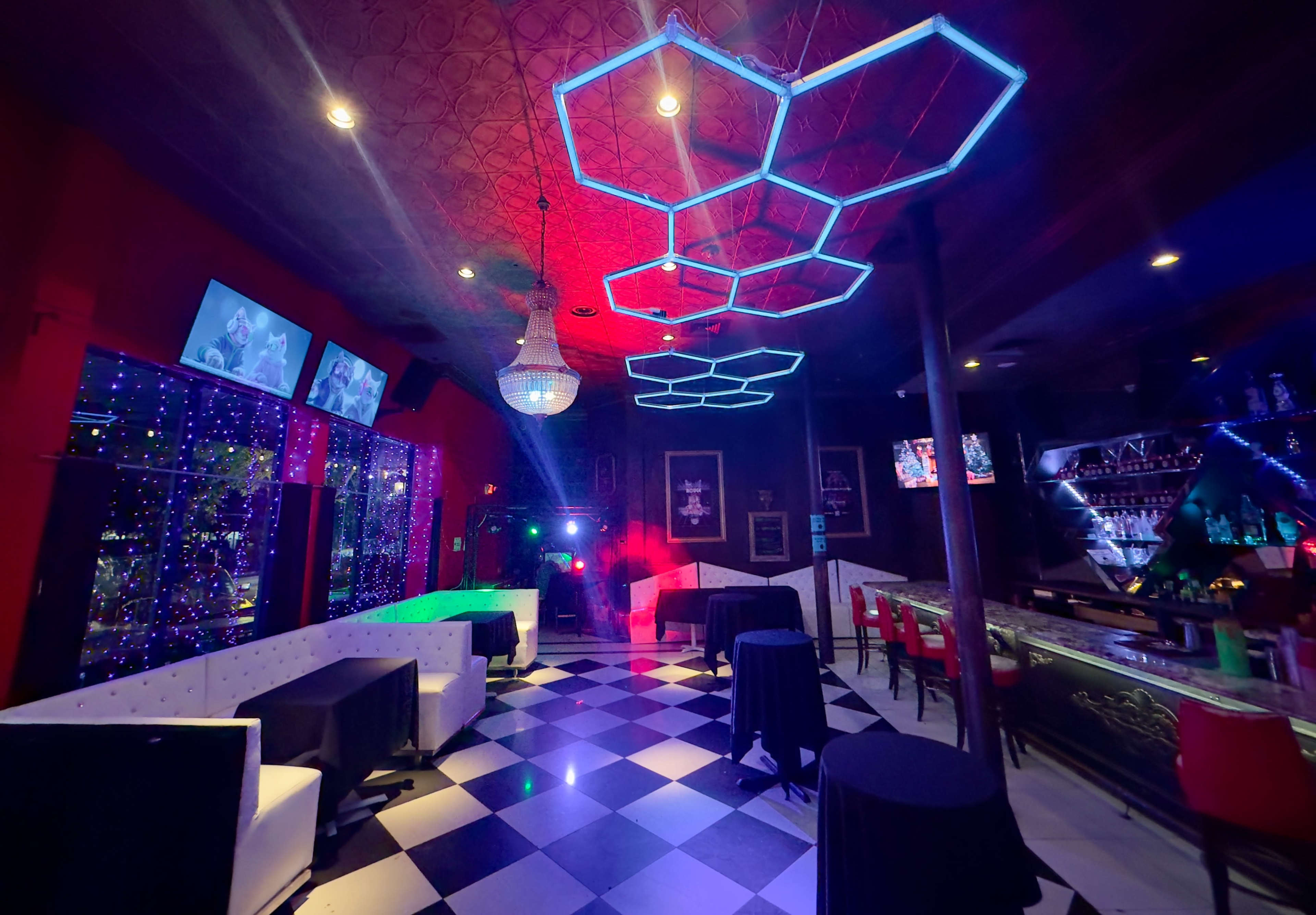 The image shows a nightclub interior with patterned black-and-white flooring, colorful lighting, and modern furniture.