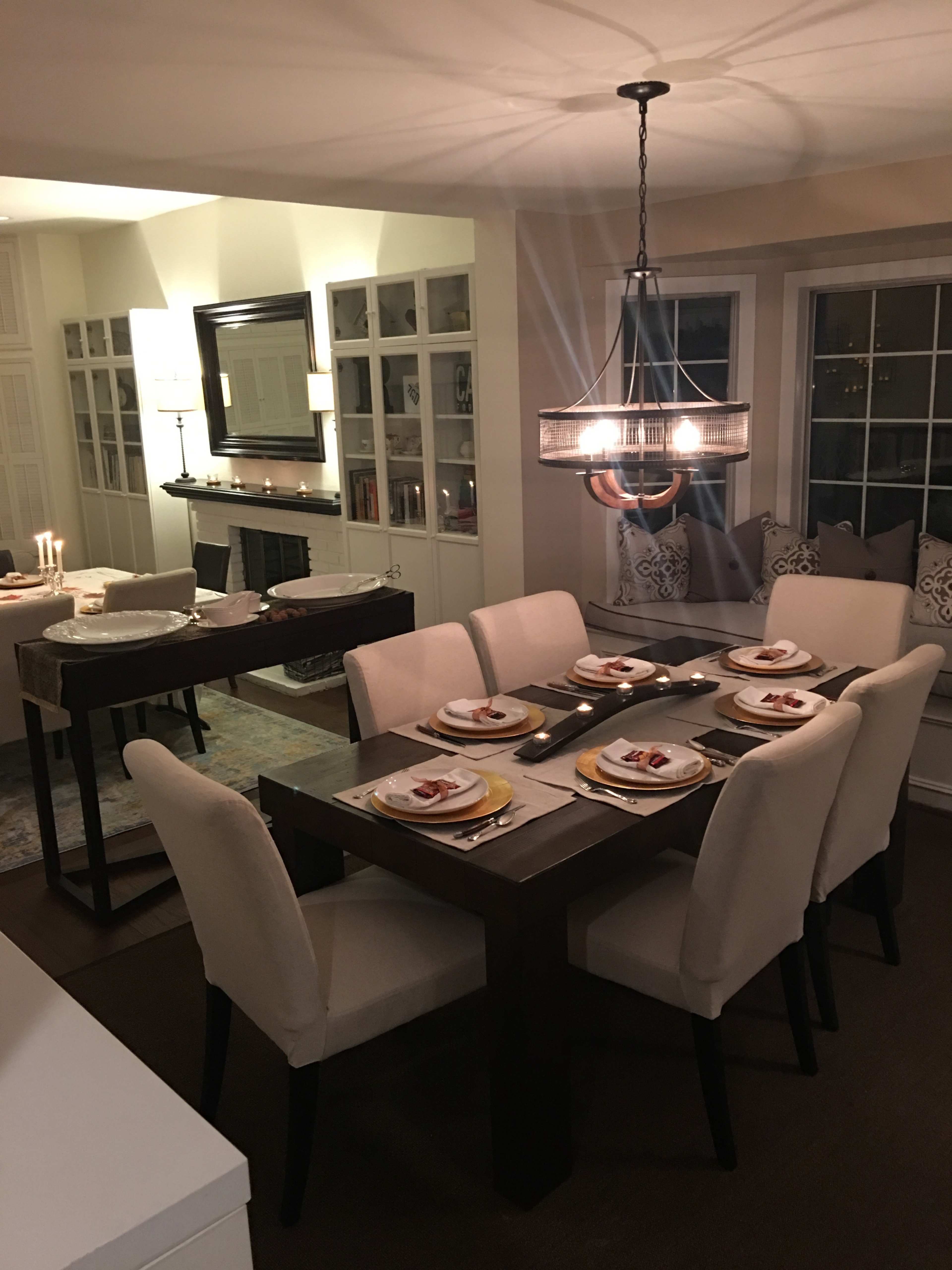 A modern dining room features a rectangular table set for dinner with cream-colored chairs, surrounded by soft lighting and decorative elements.