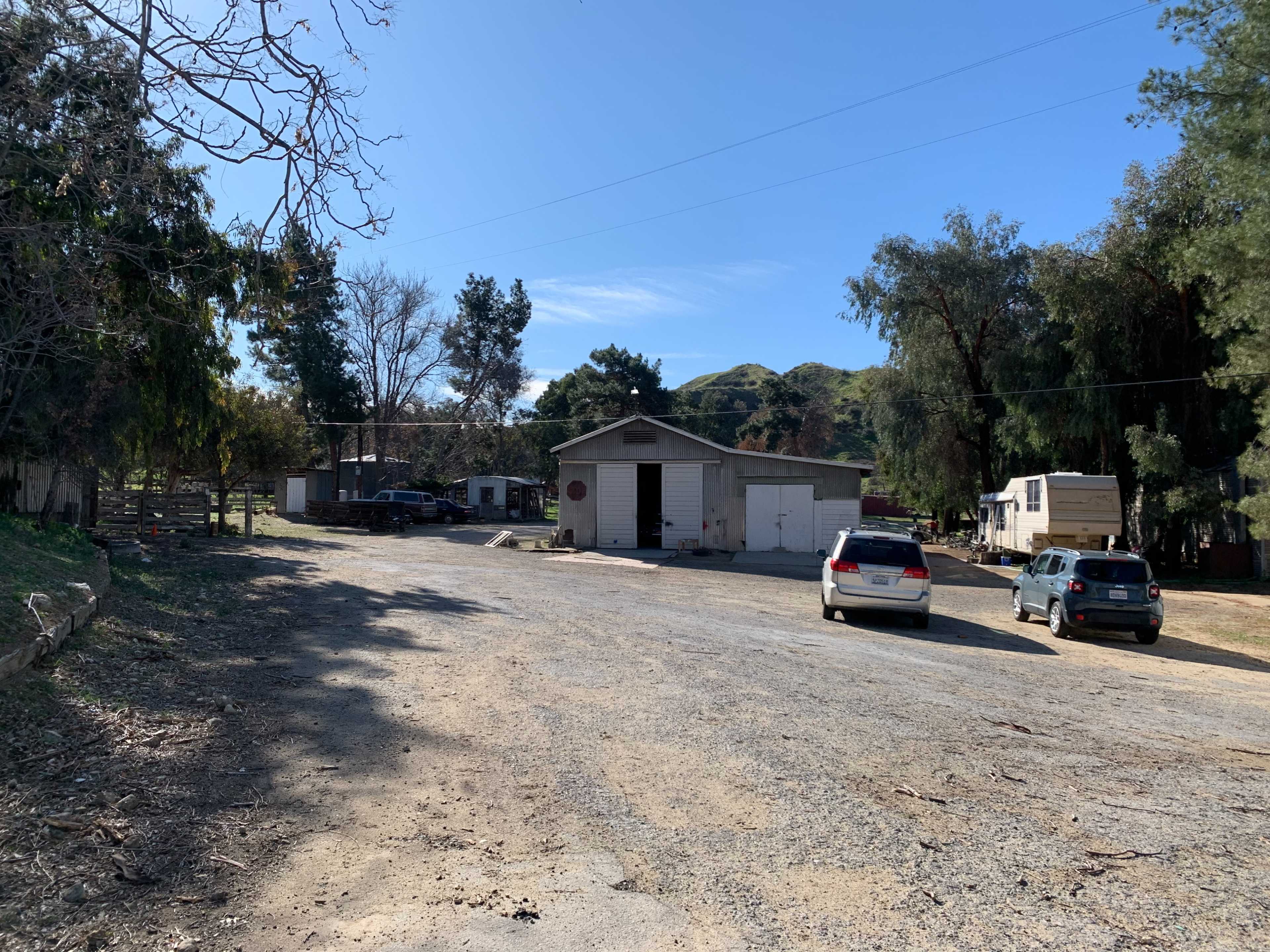 A gravel road leading to a building surrounded by trees and parked vehicles.