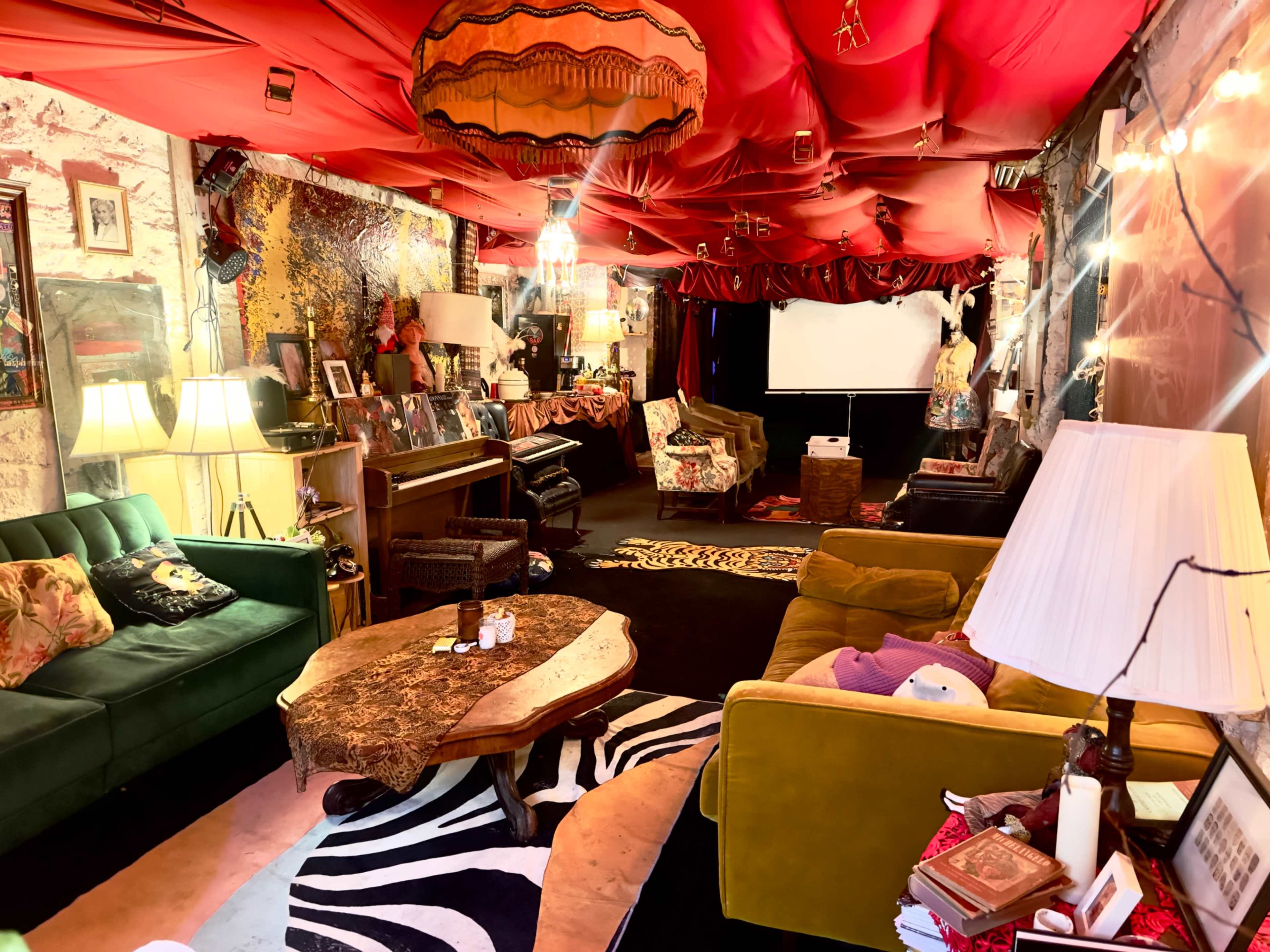 The room features a colorful interior with red draped ceilings, various seating areas, and a mix of eclectic decor.