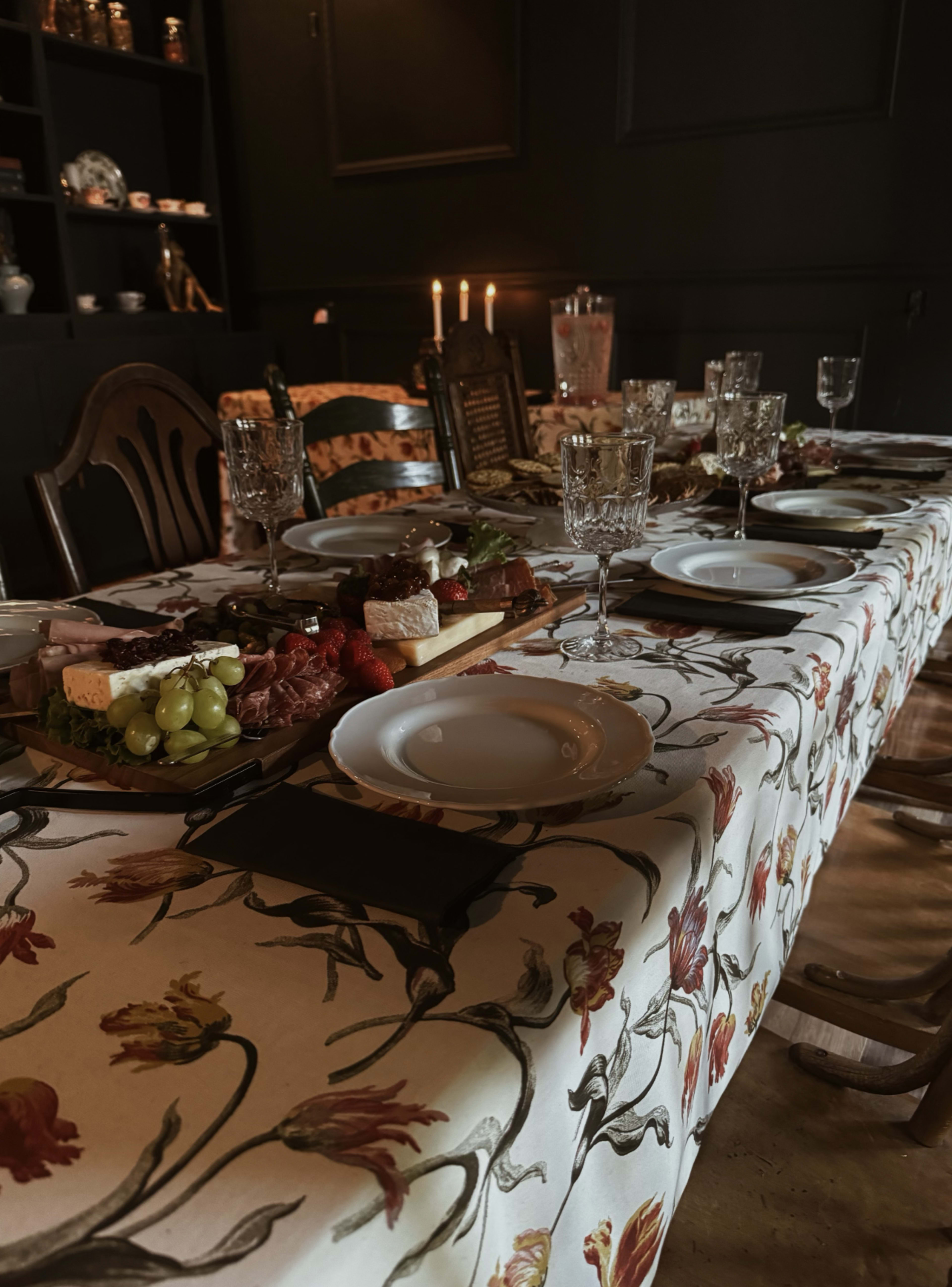 The image shows a dining table set with an elaborate spread of food, decorative tableware, and dim candlelight in a dark room.