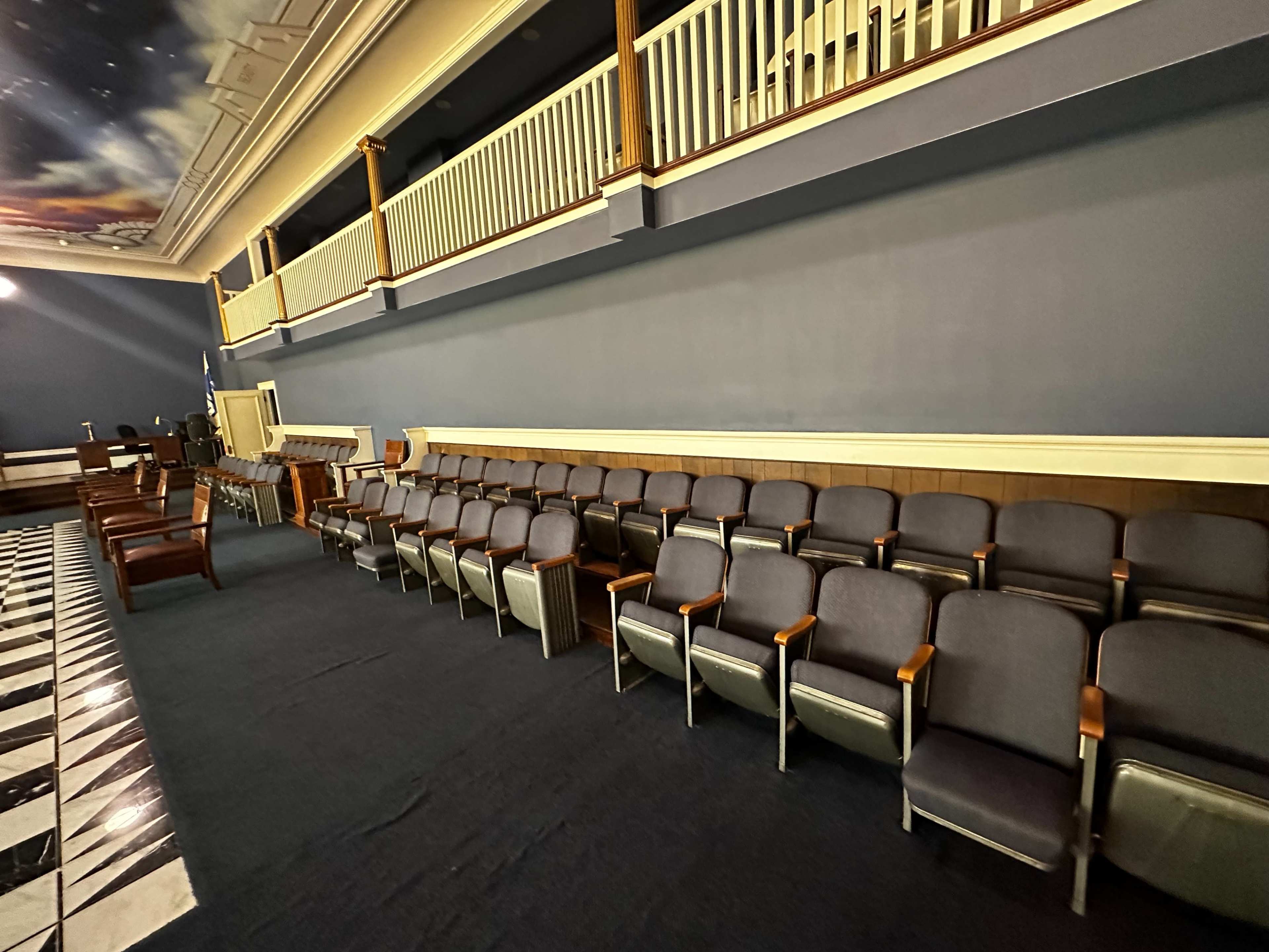 A row of upholstered chairs positioned against a dark wall in a spacious room with a checkered floor.