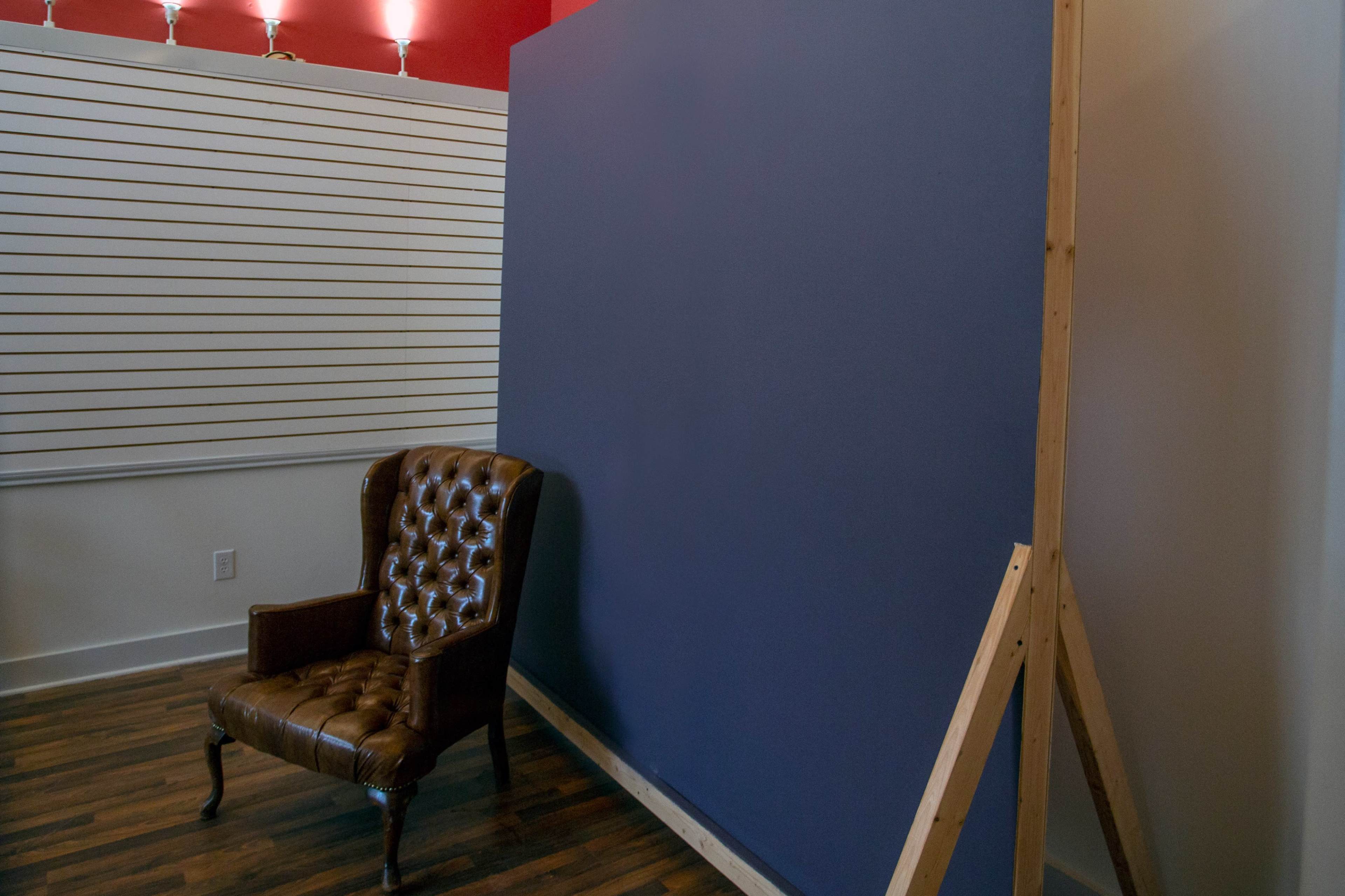 A brown leather chair is positioned next to a blue wall supported by a wooden frame in a room with hardwood flooring.