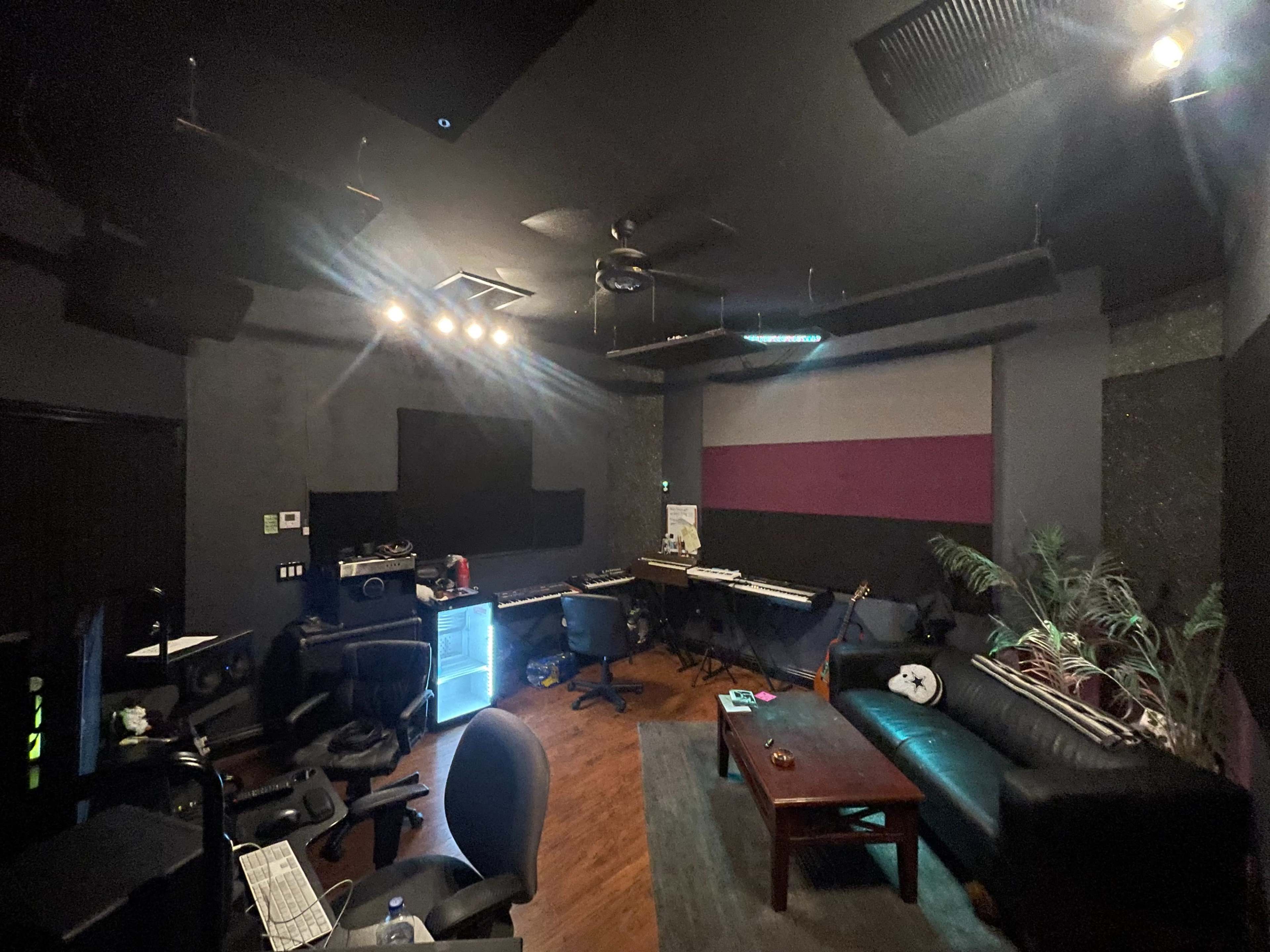 A music studio with dark walls, a desk with musical equipment, and a leather sofa in a corner.