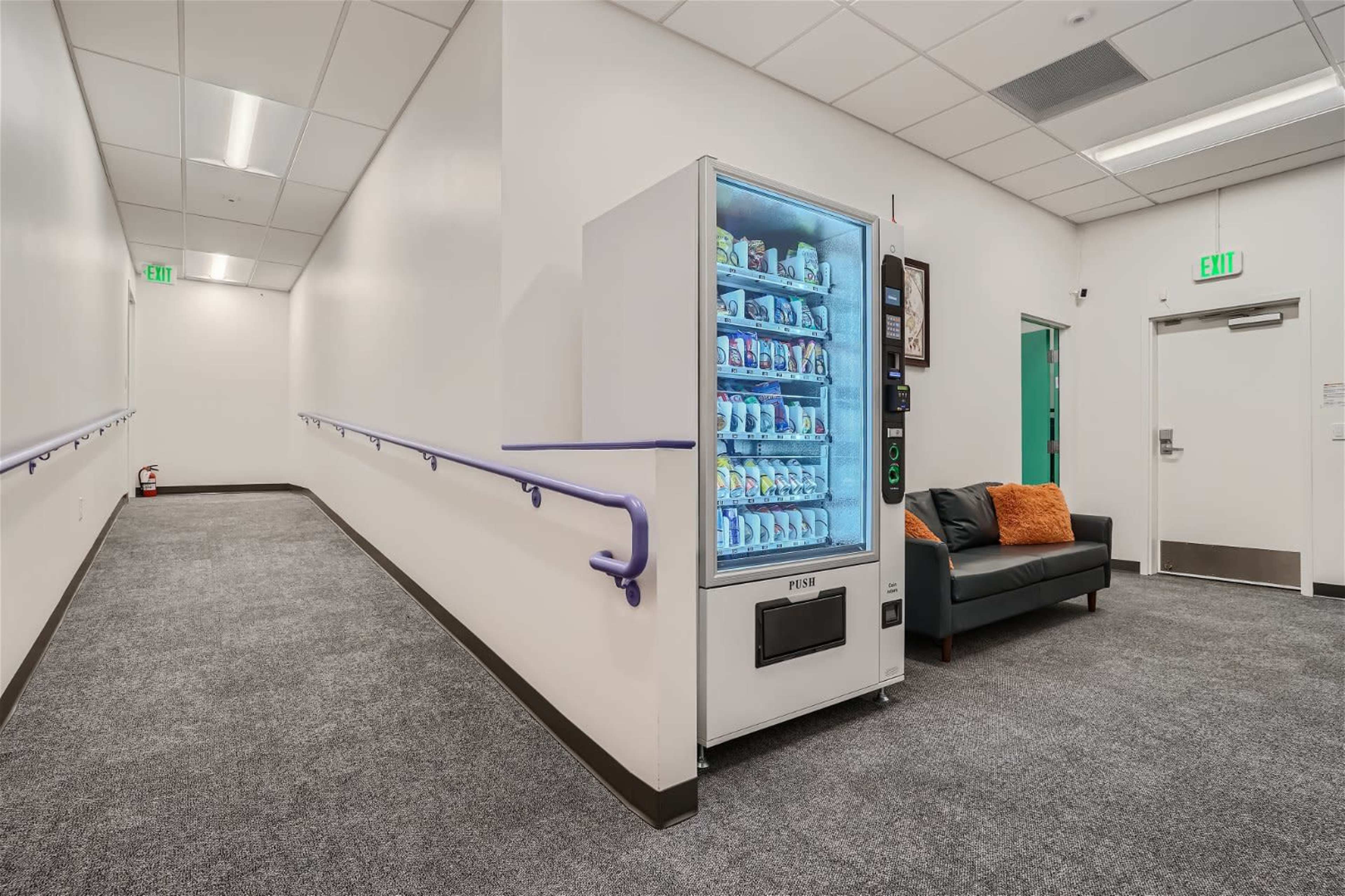 A carpeted hallway featuring a vending machine and a couch against a wall.
